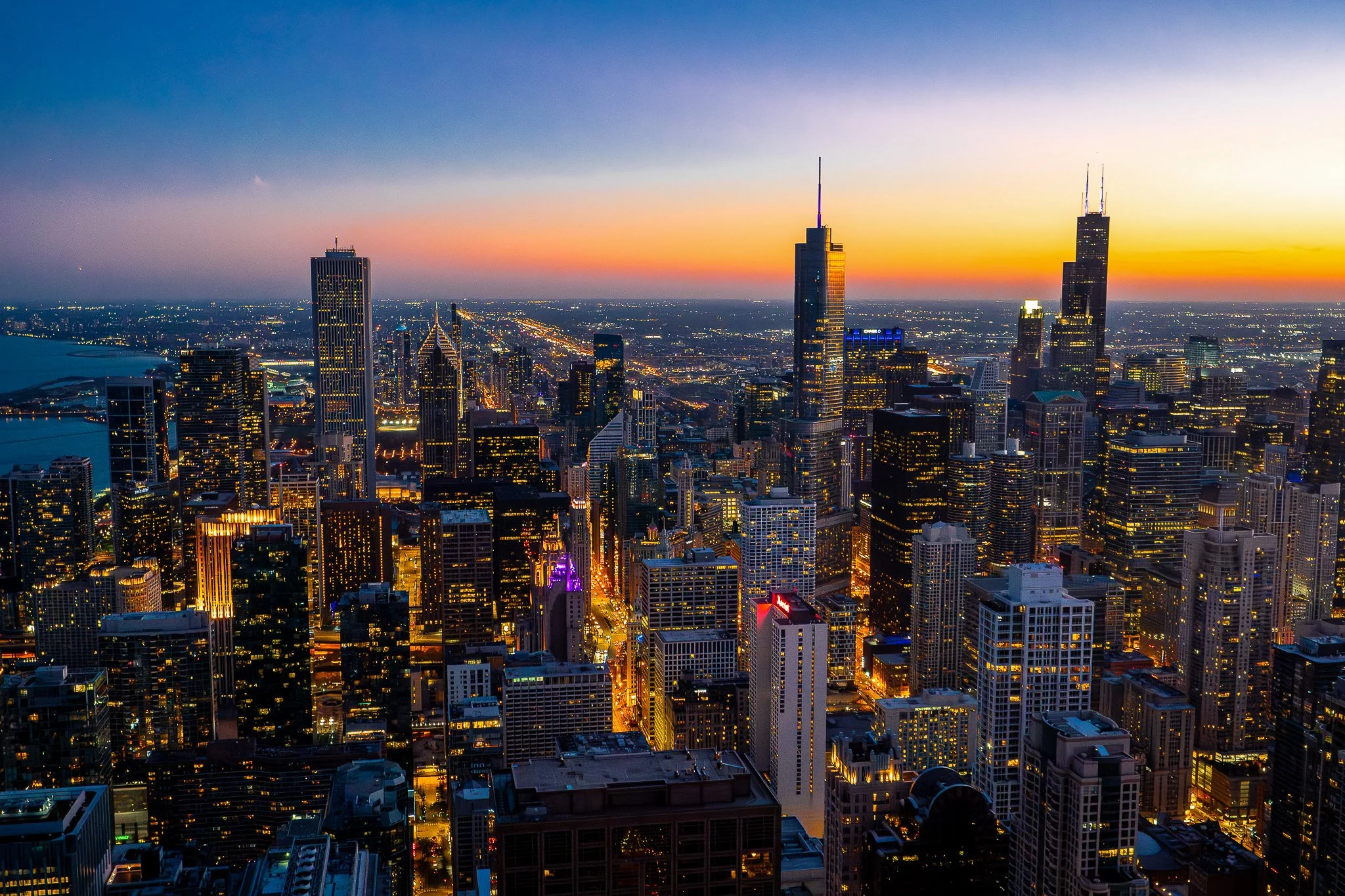 Aerial view of Chicago skyline at sunset with tall buildings, colorful sky, and city lights.