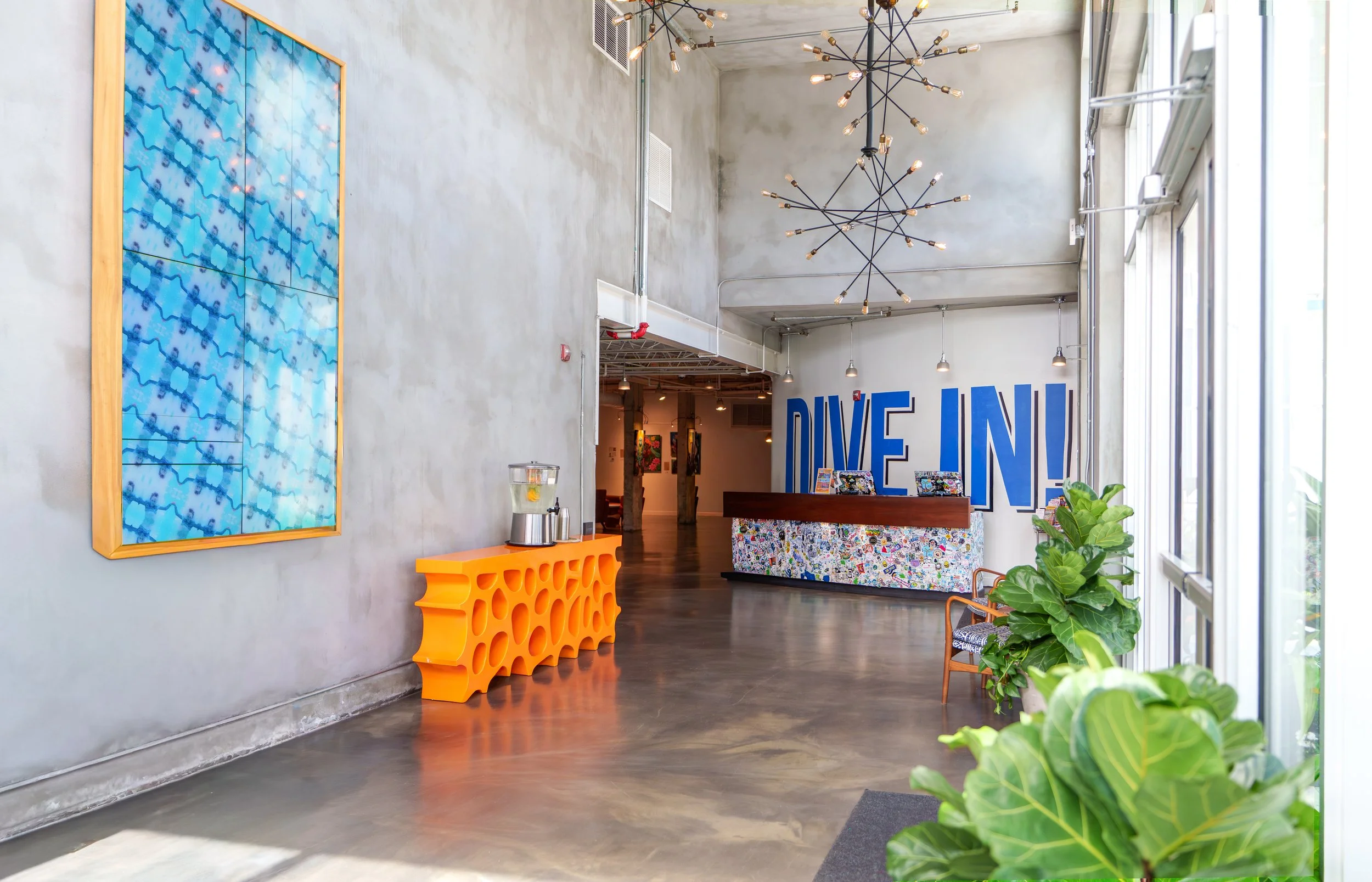 Hotel lobby interior with vibrant pool-themed art, orange console, and tropical greenery photographed for a South Florida hospitality brand