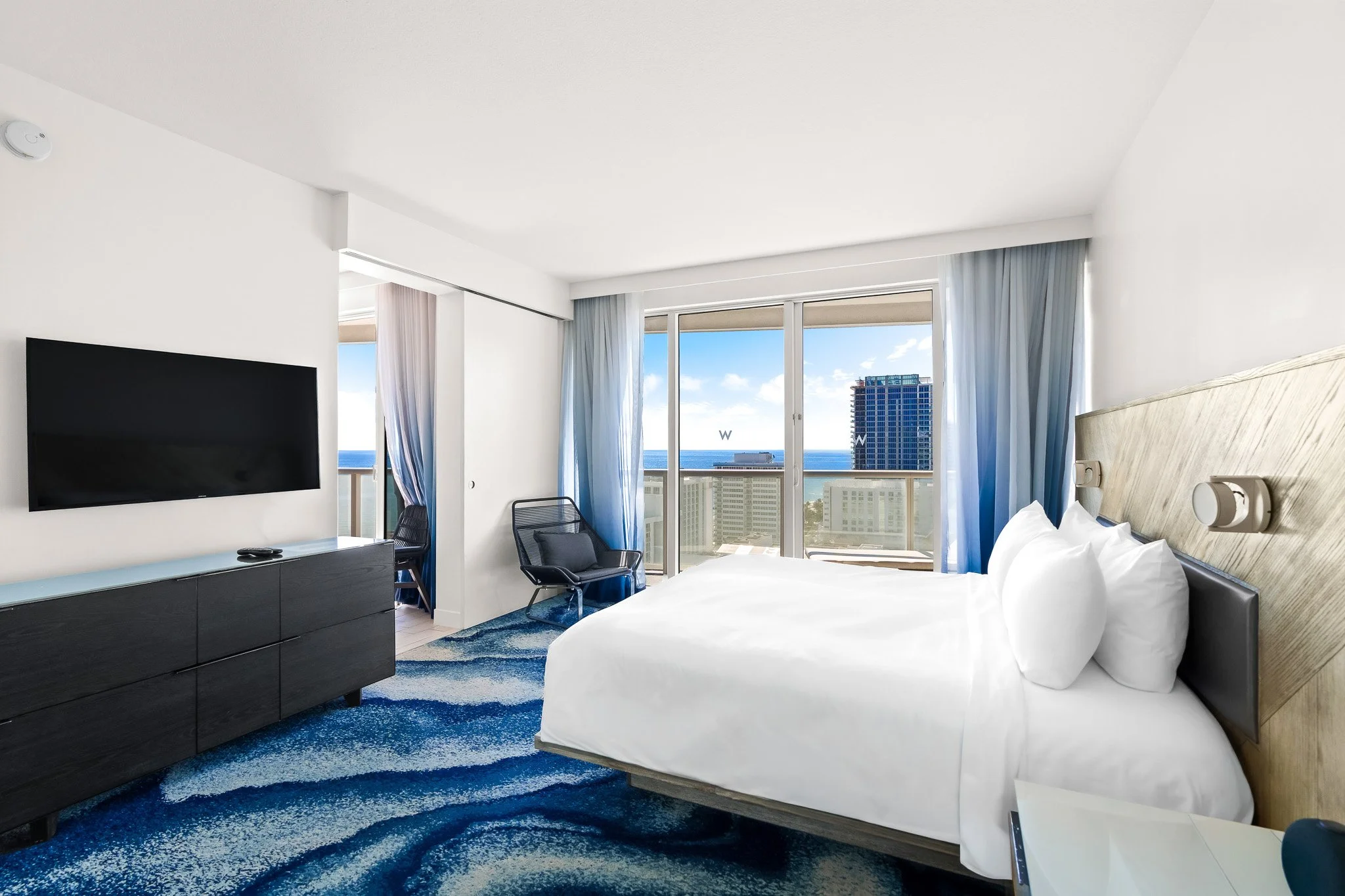 Hotel guest room with king bed, ocean view, and blue patterned carpet at a South Florida resort