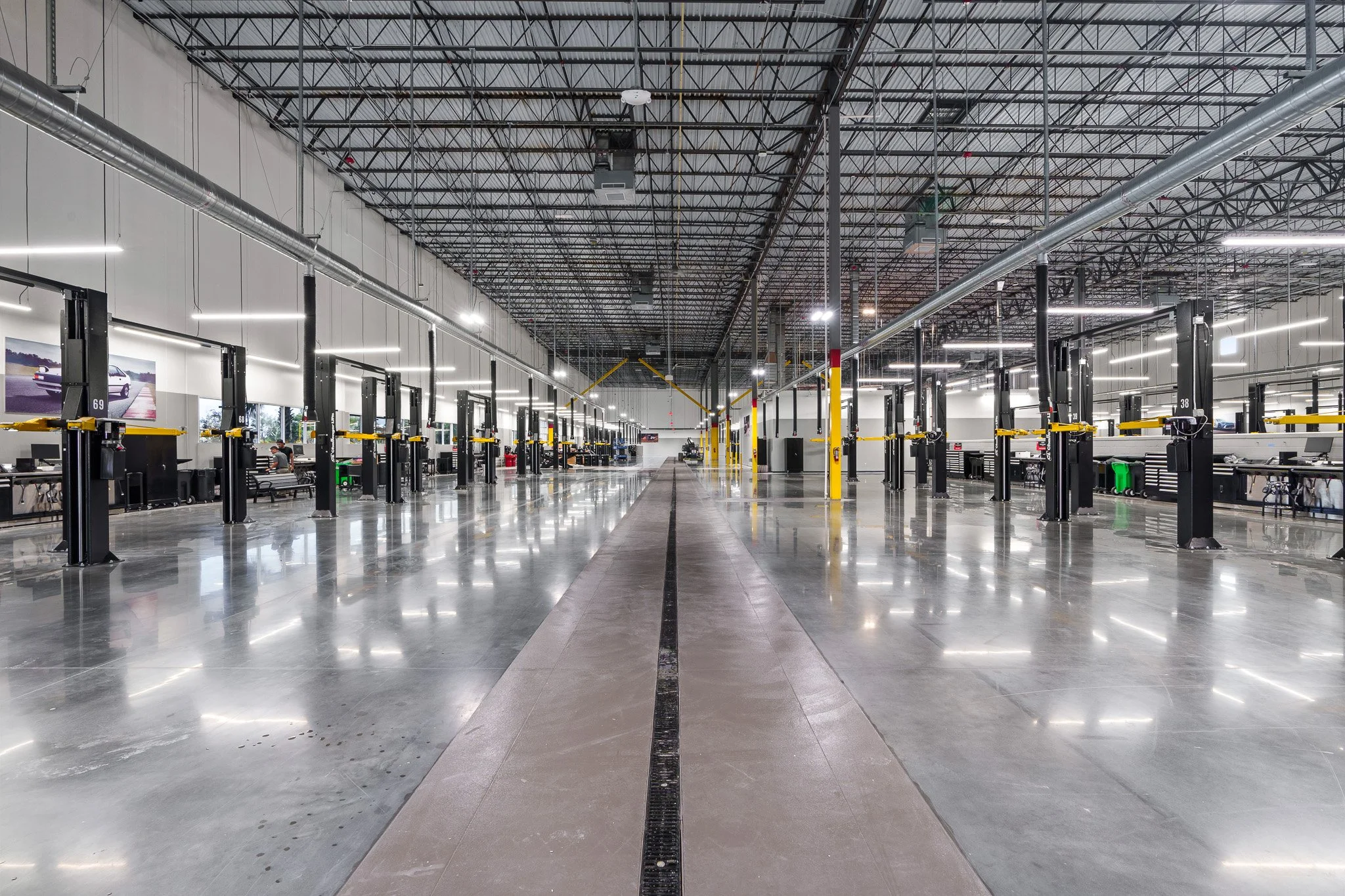 An empty, spacious automotive service workshop with multiple vehicle lifts, shiny concrete floors, and a high ceiling with metal framing and ductwork.