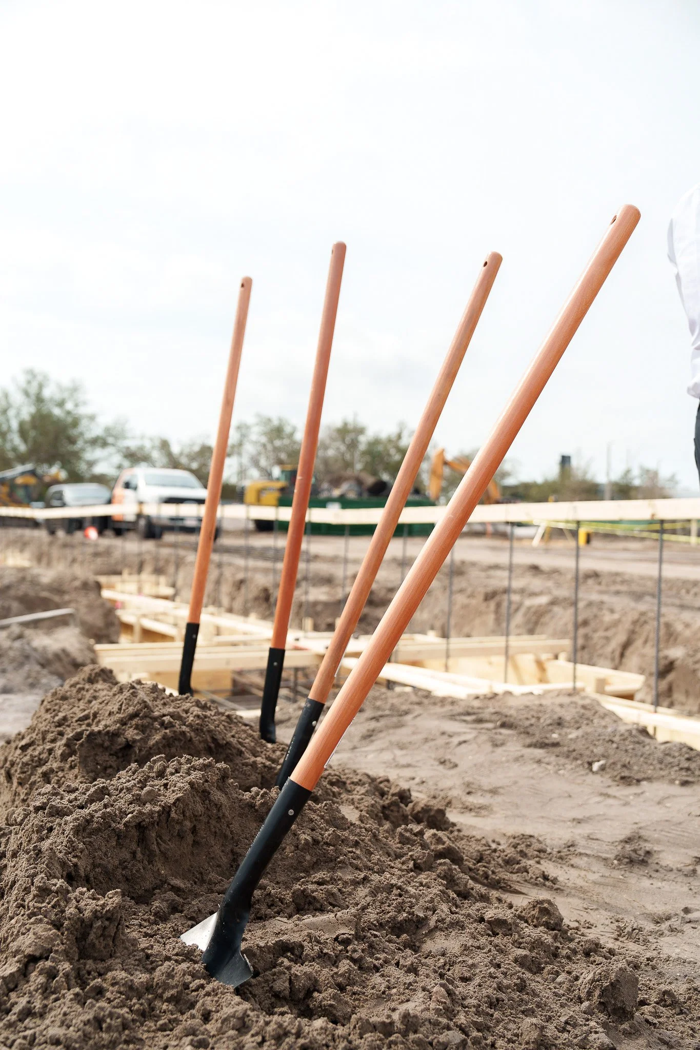 Shovels planted in soil at a construction site with dirt and a partially built framework in the background.