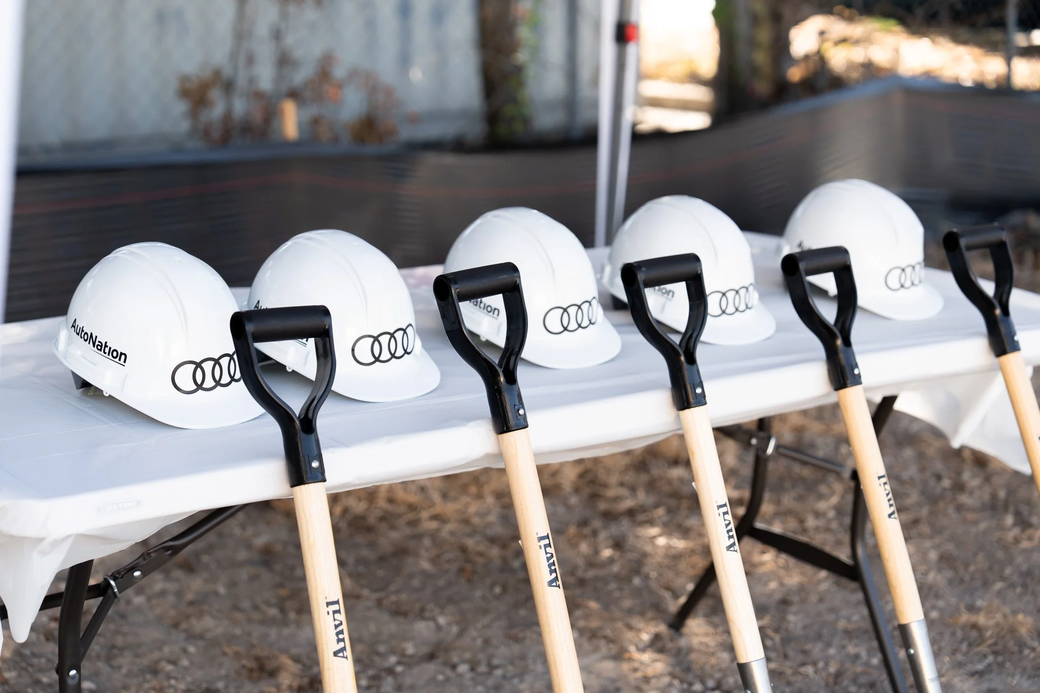 White safety helmets with the Audi logo and shovels are lined up on a table outdoors, likely for a groundbreaking event.