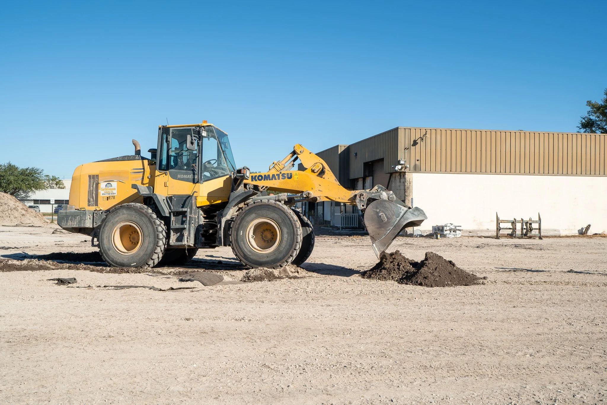 A yellow Komatsu front loader moving dirt on a construction site with a building and blue sky in the background.