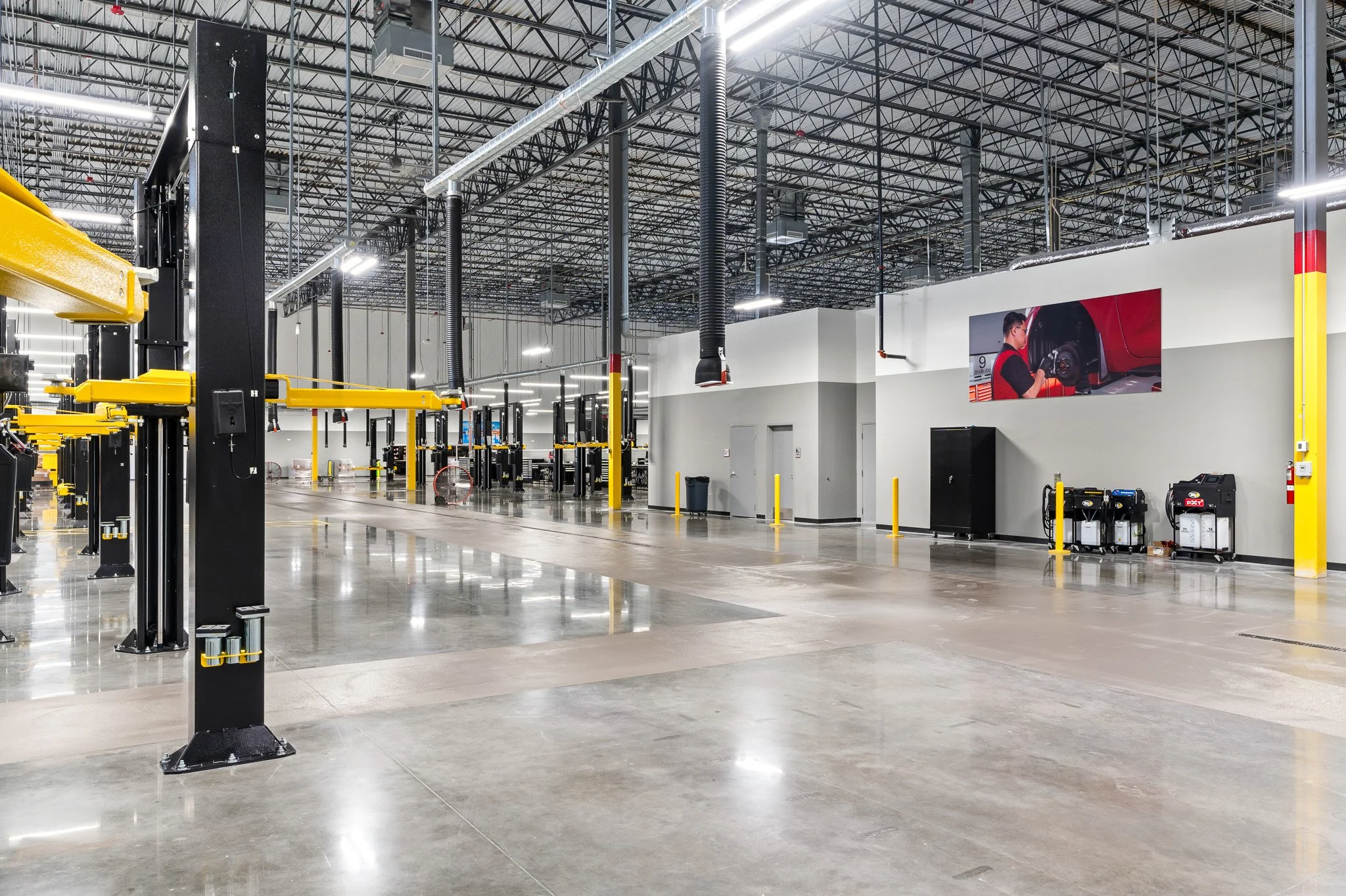Interior of an empty automotive service or repair shop with large open space, high ceiling, and various equipment and work stations visible.