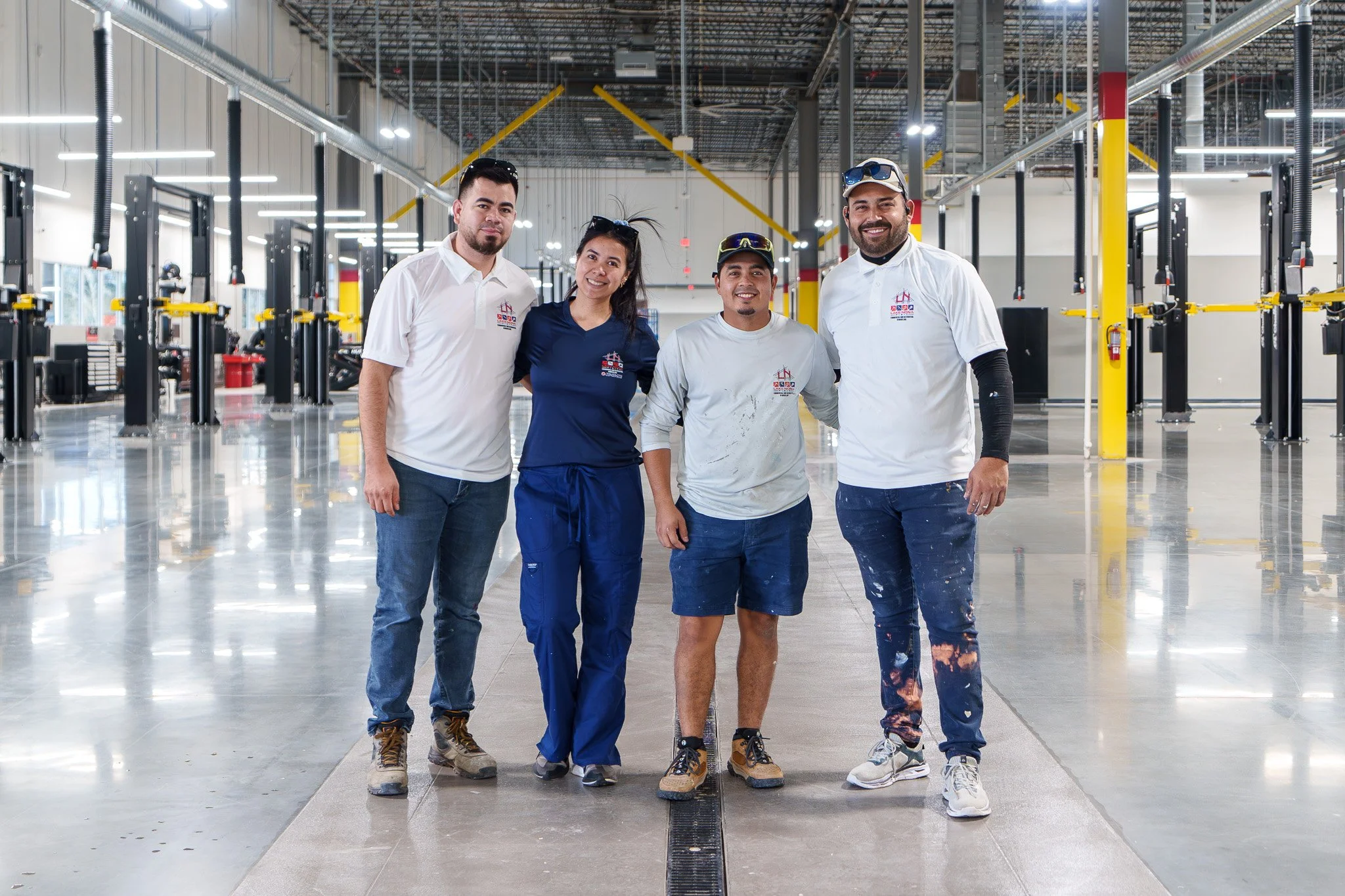 Group of four diverse workers standing inside a modern industrial or manufacturing facility, smiling and posing for the photograph.