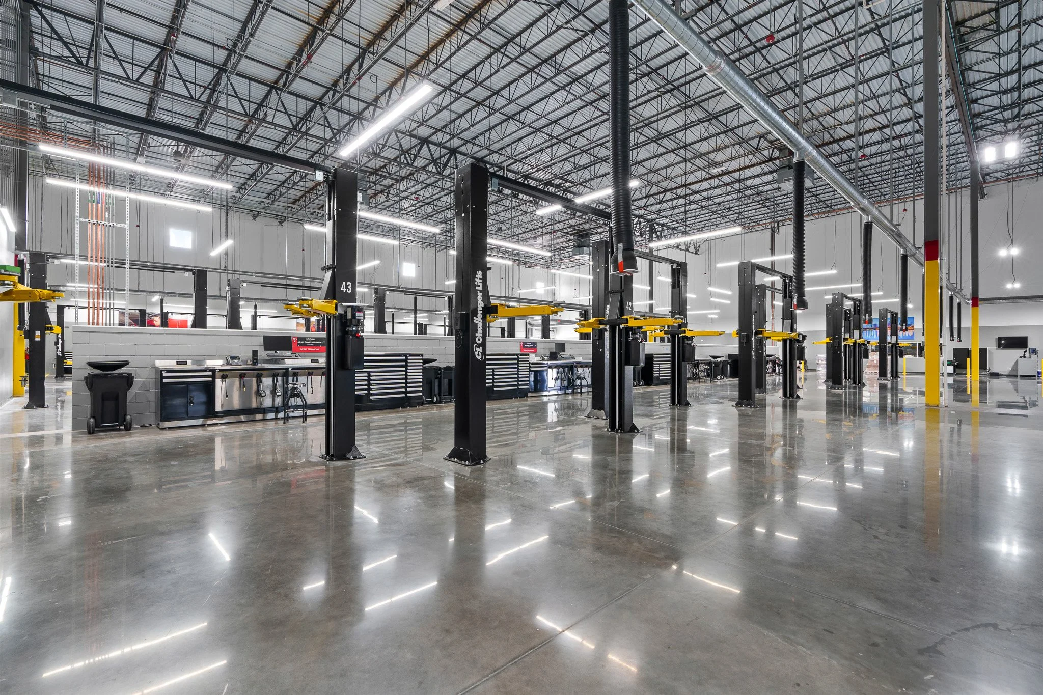 Empty vehicle service or repair garage with car lifts, workstations, and a polished concrete floor.