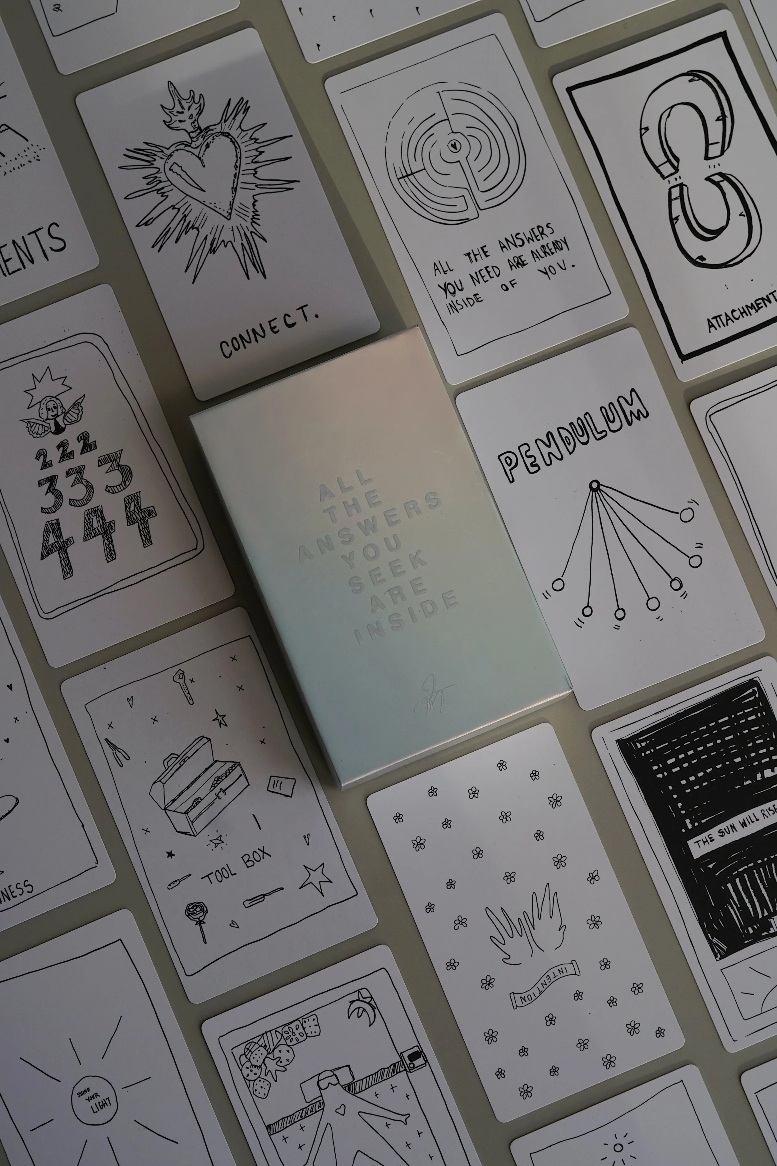 A collection of black and white tarot or oracle cards spread out on a surface, with a small white box in the center that reads 'All the answers you seek are inside.'