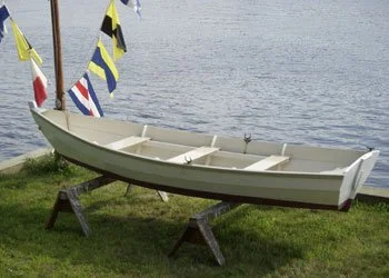 A white Merrimack skiff with red bottom paint sits at the edge of the water on to short saw horses.