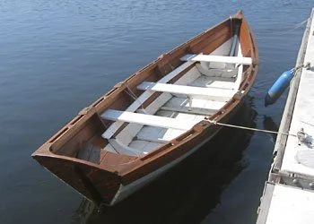 A Salisbury Point Skiff tied to a dock with varnished sternsheets, white thwarts and bilge.