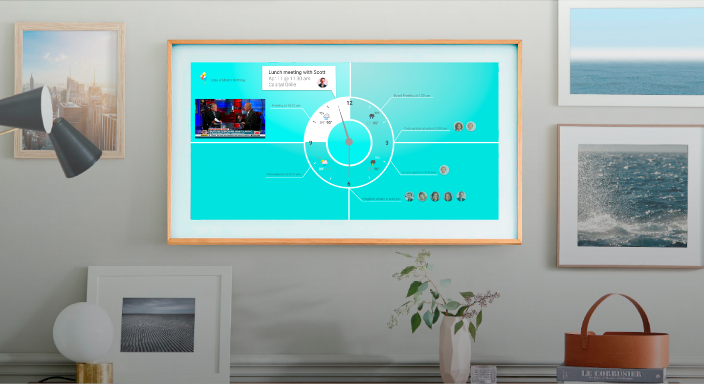 A Samsung Frame TV mounted on a living room wall displaying a teal dashboard UI with a clock, calendar event, news feed, and contact avatars