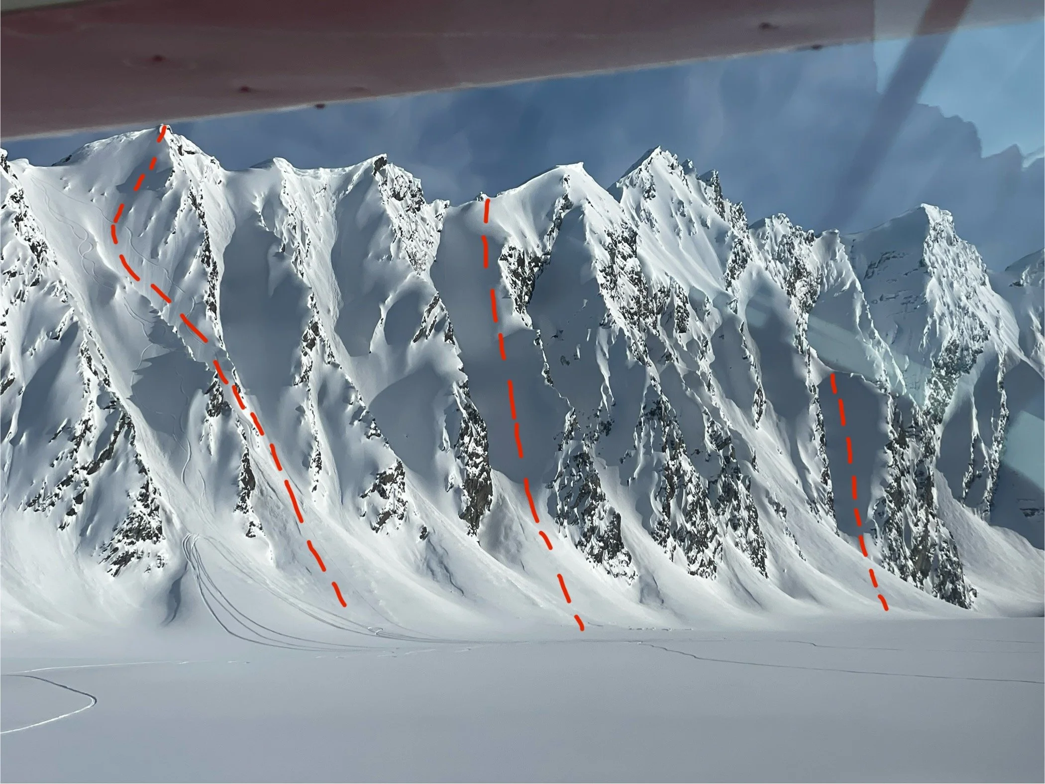 Ski lines are marked with red dotted lines down steep mountain faces and chutes