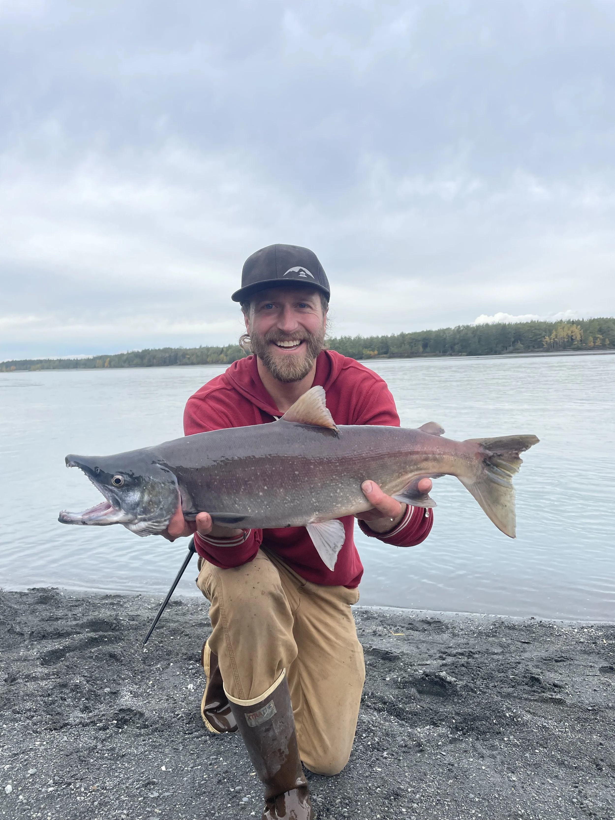 A man holds a Salmon fish caught on the Knik River which sits in the background of the photo
