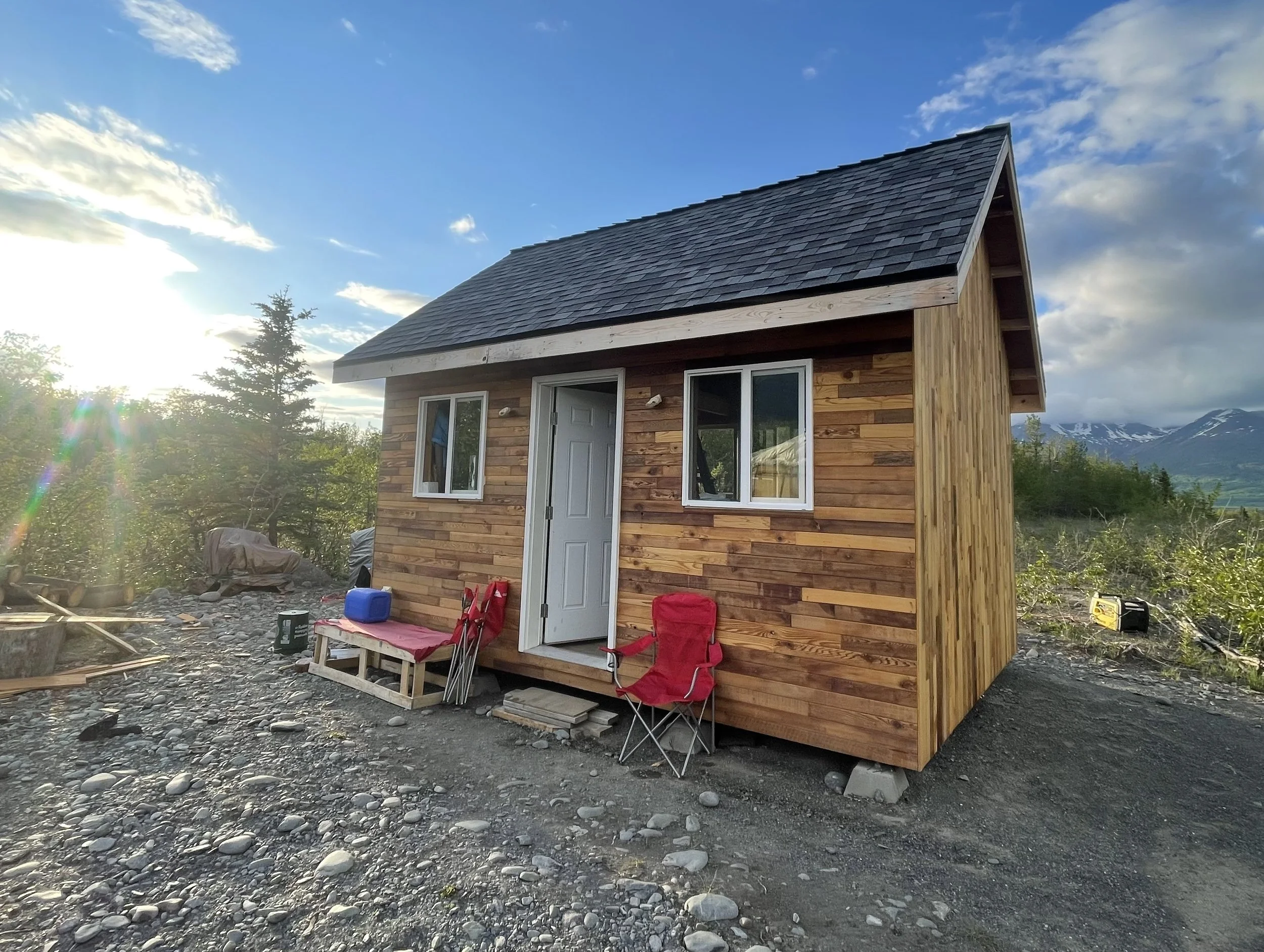 A cedar lined tiny house with an open door and camp chairs set up outside