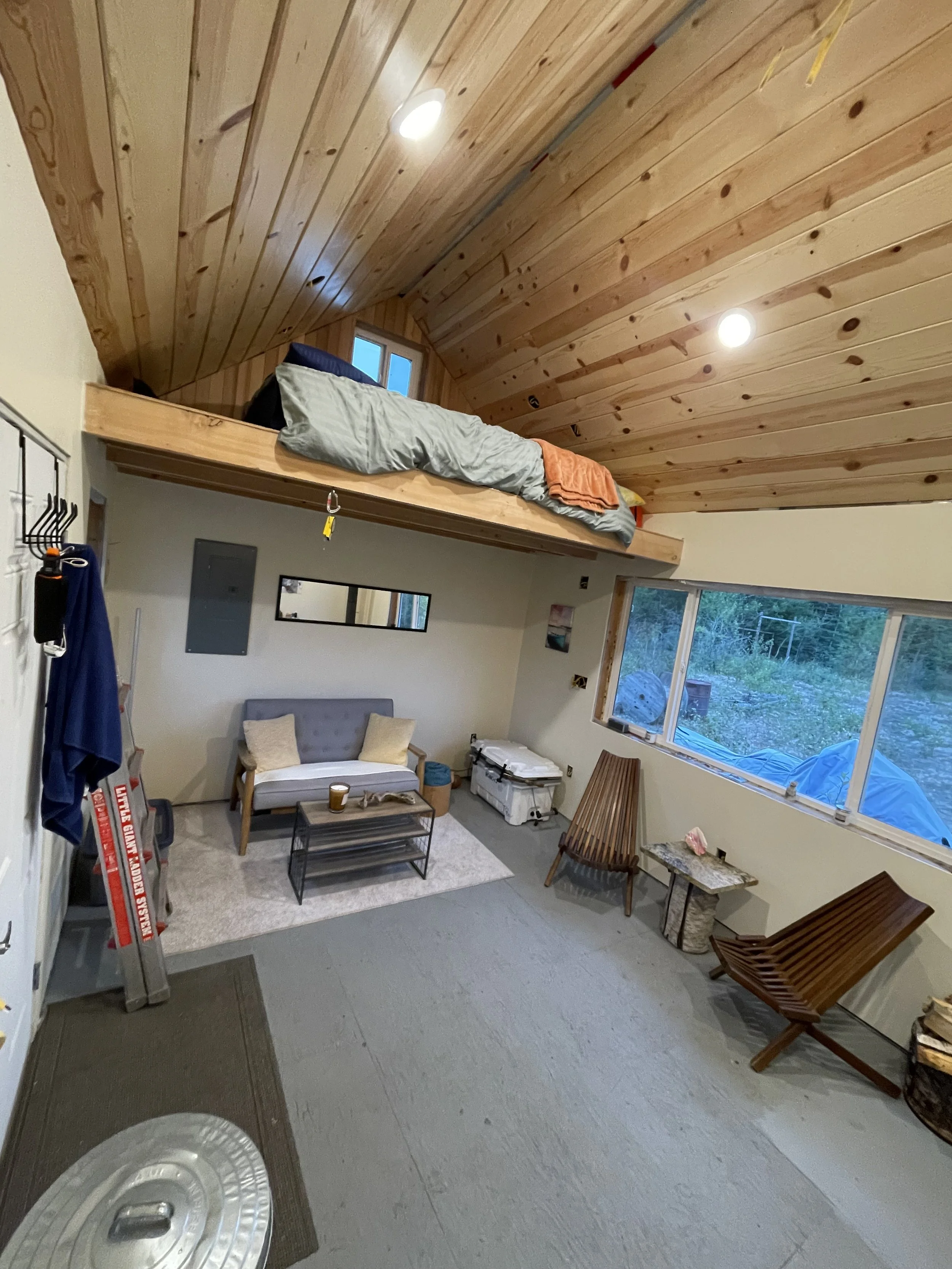 Inside view of a tiny house showing the couch in the living room and upstairs loft and bed