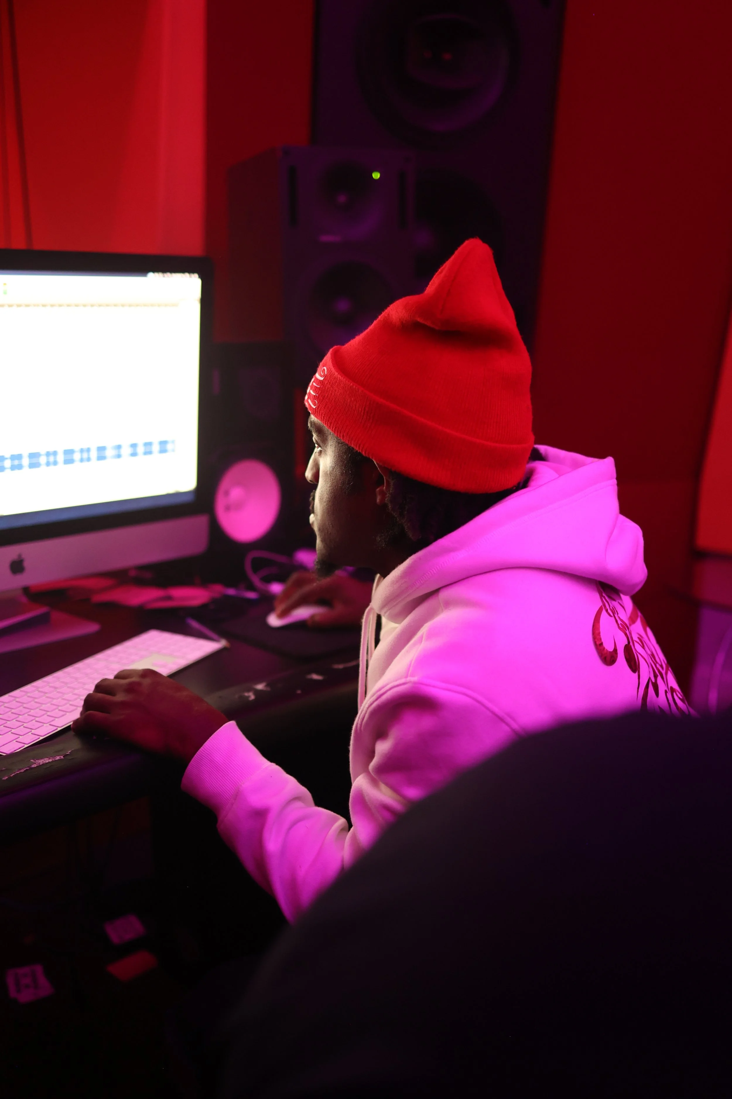 Independent artist producing music at a computer in a red-lit recording studio during an immersive creative camp focused on artist development.
