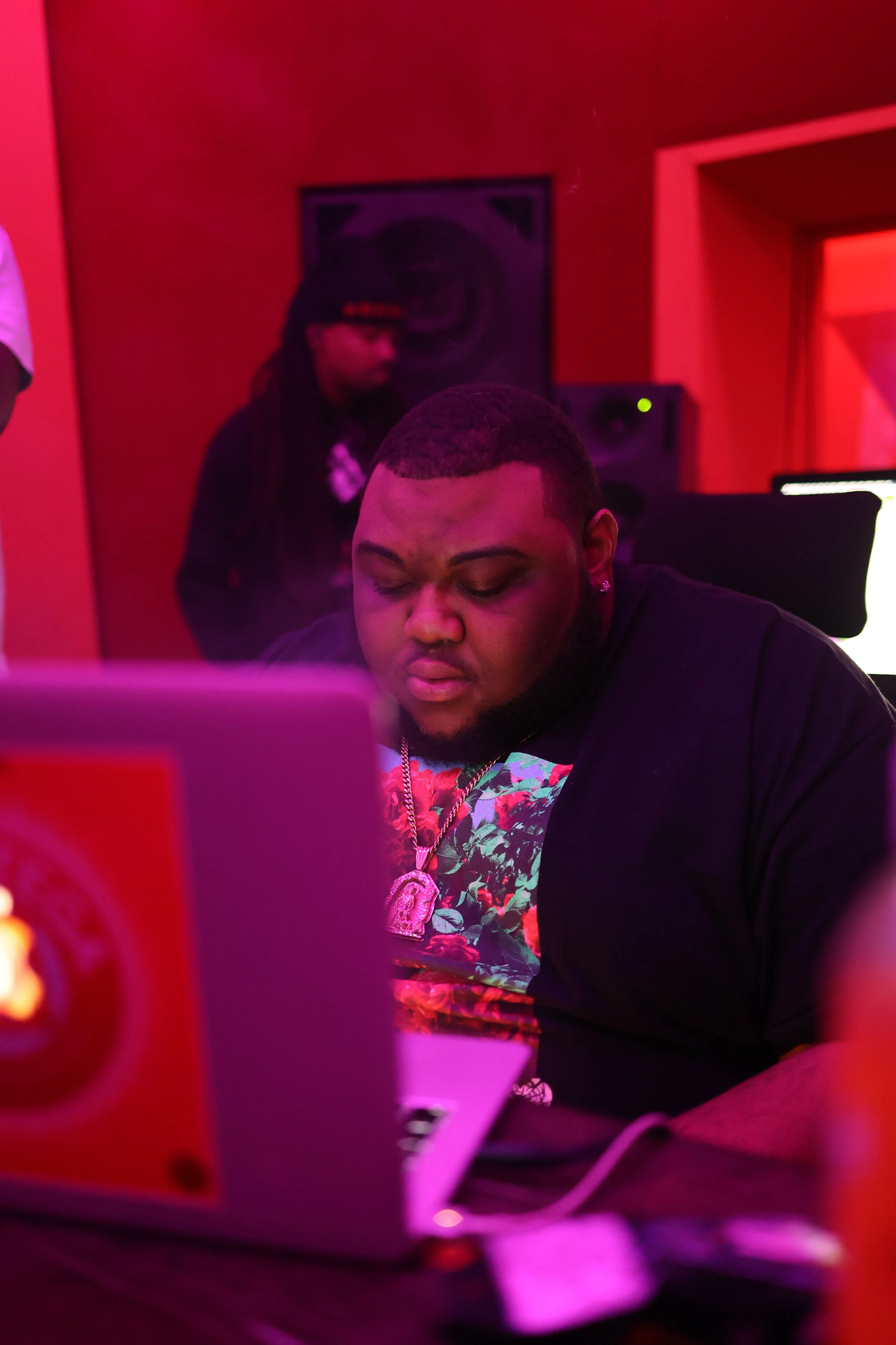 Independent artist working on music at a laptop in a red-lit recording studio during an immersive creative camp focused on collaboration and artistic development.