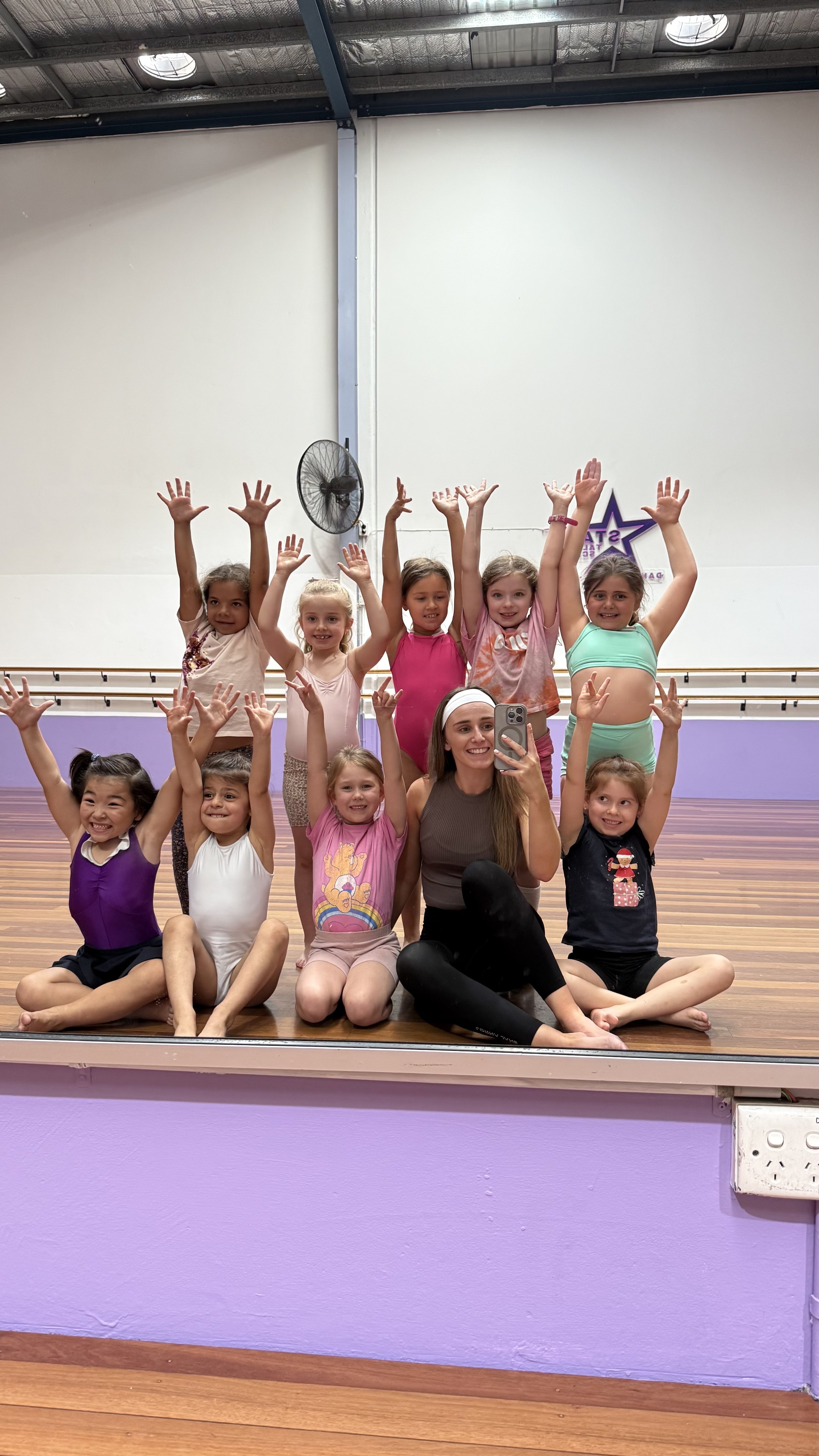 Group of young girls in colorful dance costumes standing together in a dance studio.