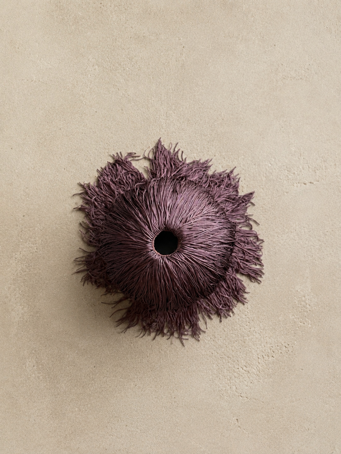 Bordeaux Noir Spill Sphere Vessel with cascading fringe holding burgundy flowers against a warm neutral background.