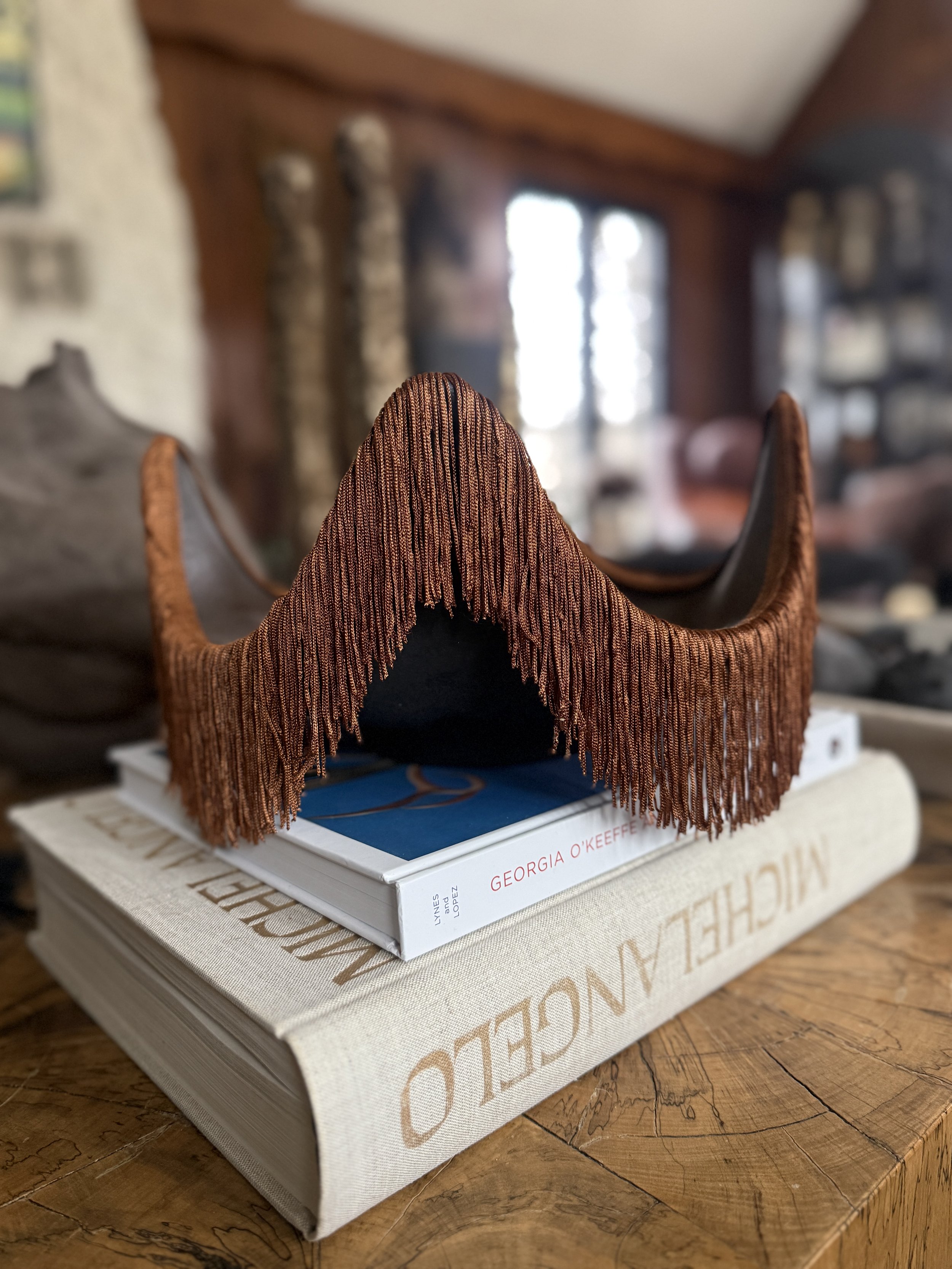 A sculptural catchall tray with a warm cayenne tone, featuring a wavy silhouette and fringe detail, set against a neutral studio background.