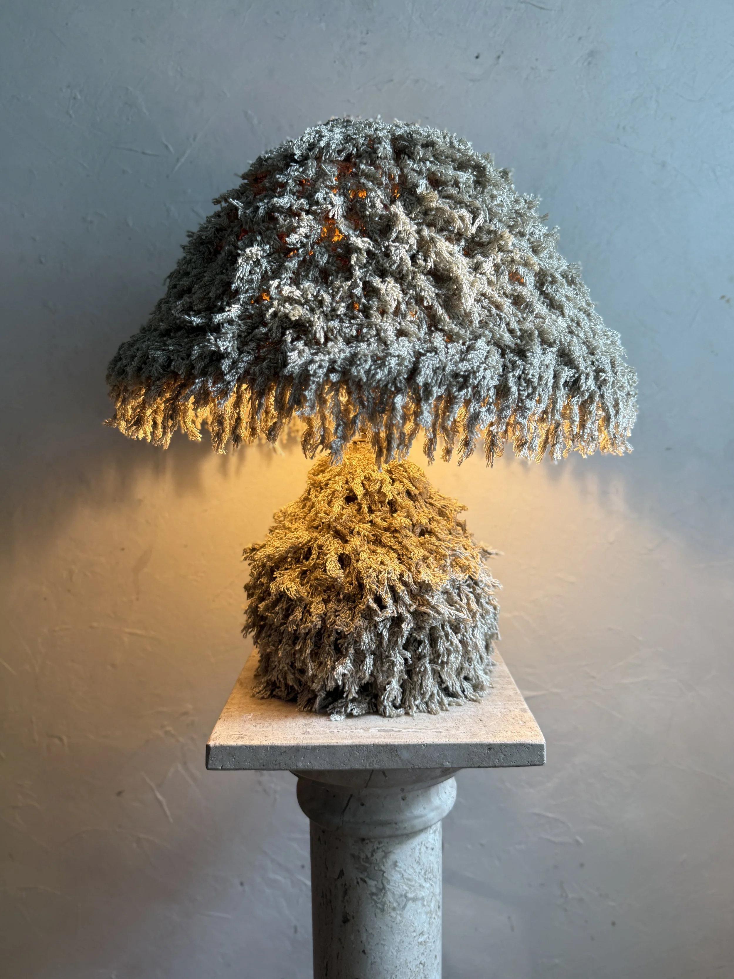 Soft Moss Shag Lamp by Amber Renee Hansen — sculptural fringe-wrapped mushroom lamp in moss tones glowing warmly.