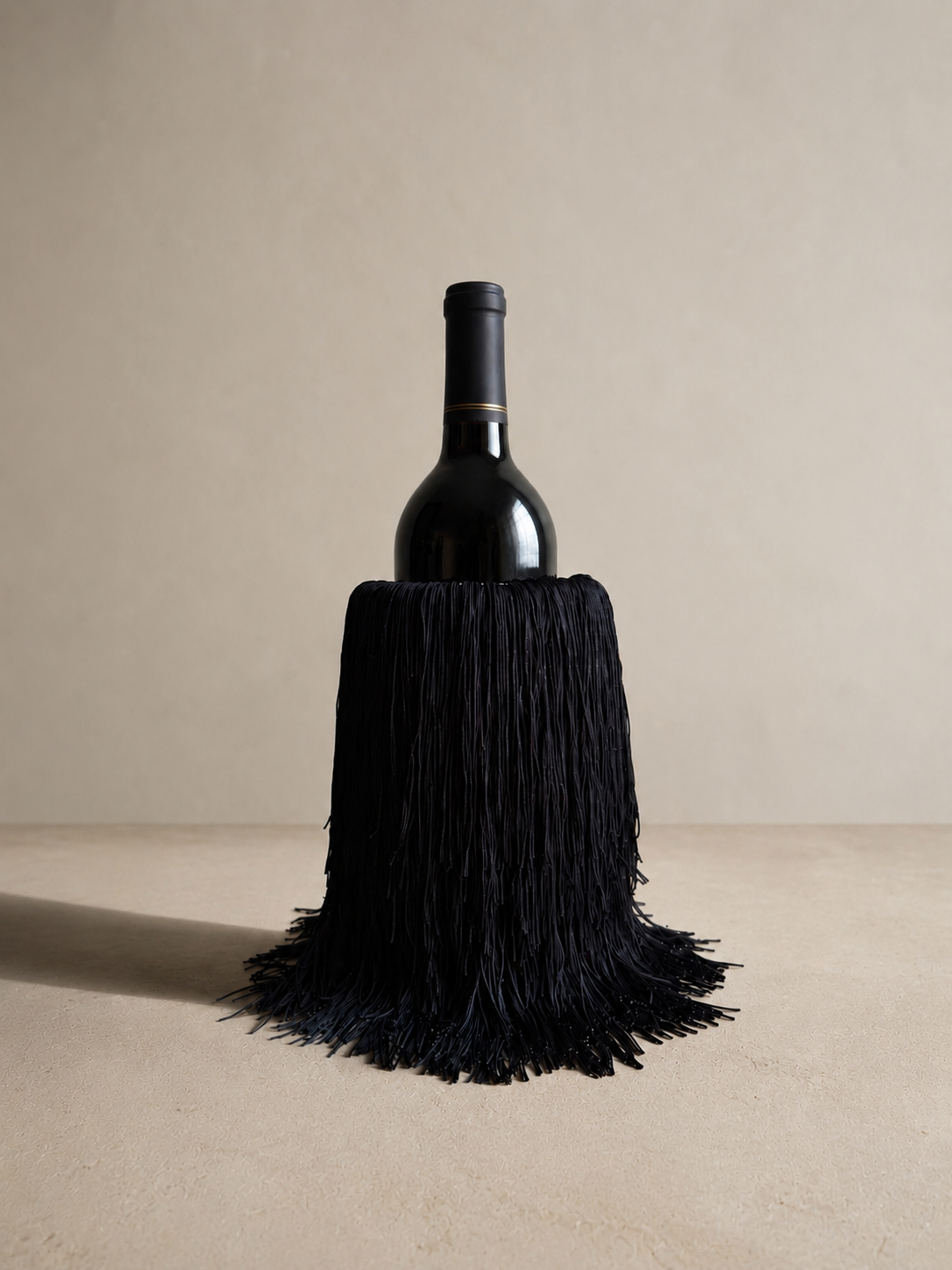 A white marble wine chiller fully wrapped in hand-finished black fringe, serving as a striking, designer-forward wine cooler.