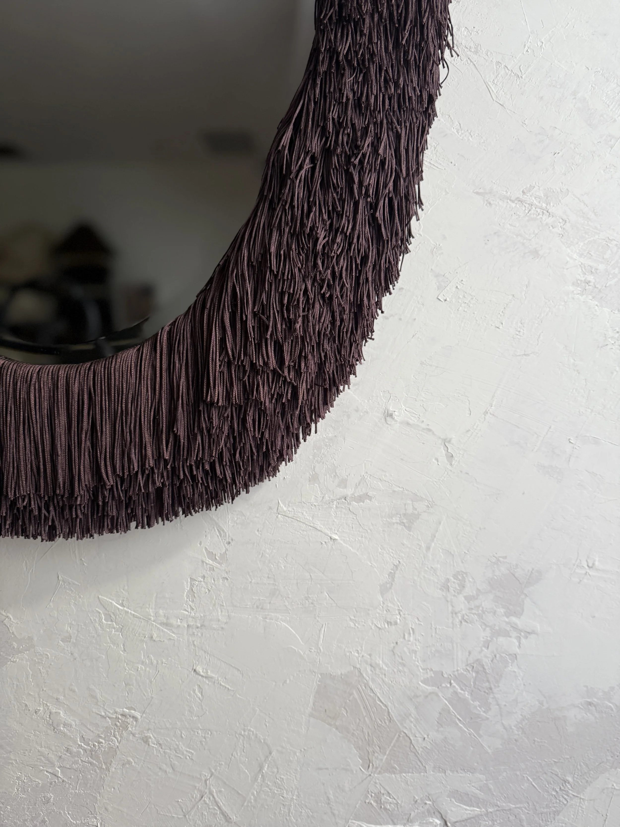 Oval mirror wrapped in rich, dimensional fringe.