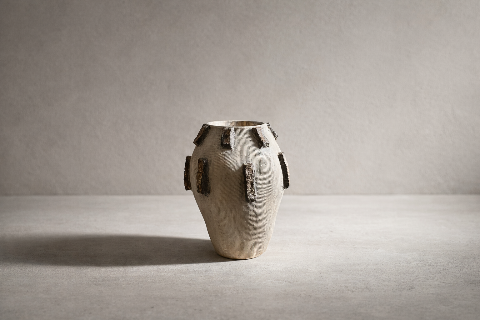 Neutral elongated vessel with raised bark-style relief accents on a textured surface