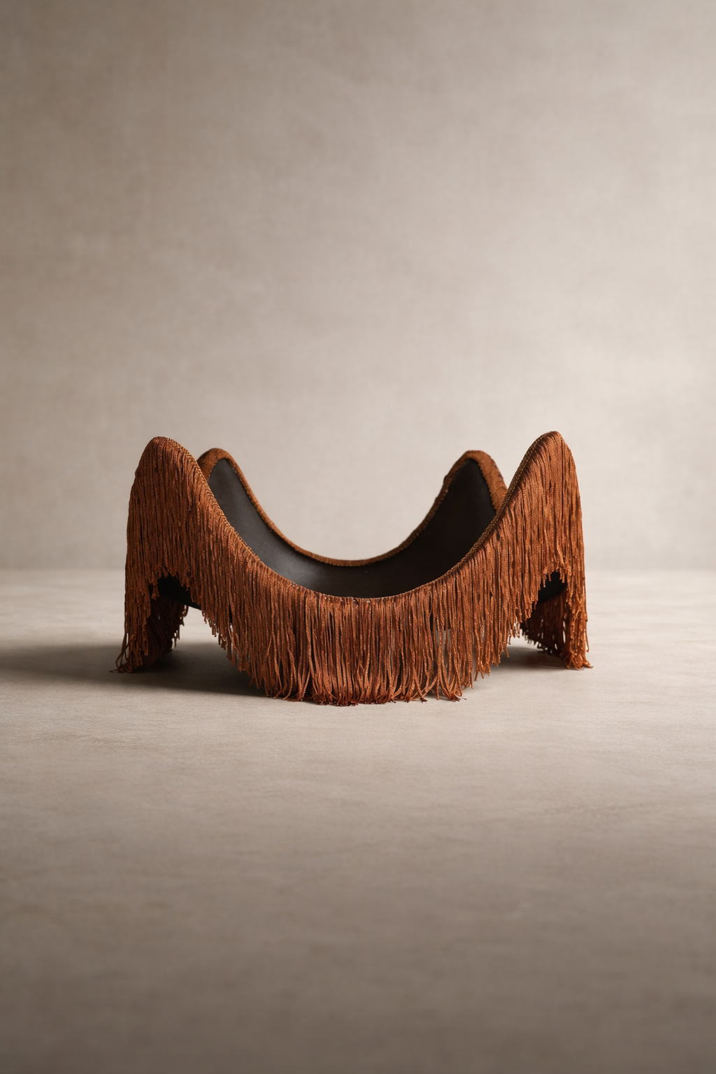 A sculptural catchall tray with a warm cayenne tone, featuring a wavy silhouette and fringe detail, set against a neutral studio background.