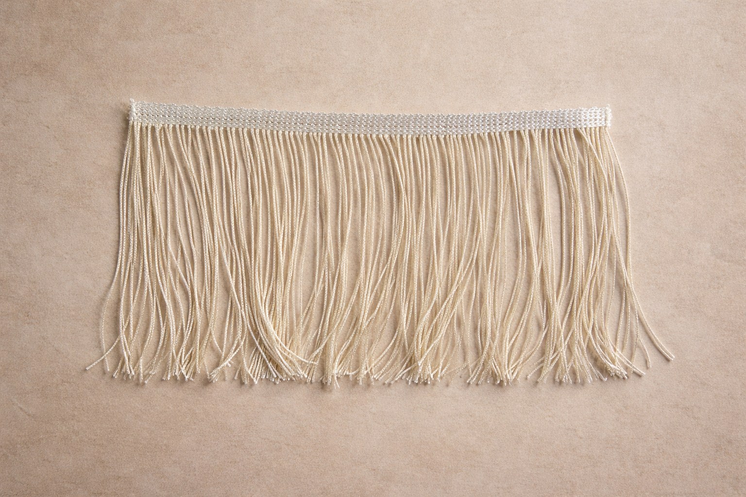 Cream “Quiet Bone” fringe trim in a close-up overhead view, featuring soft twisted strands with a subtle sheen on a warm neutral surface.