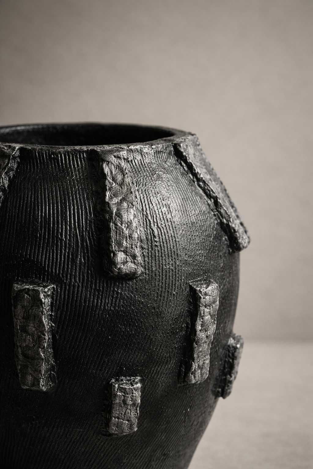 Black elongated vessel with raised bark-style relief accents and matte textured finish