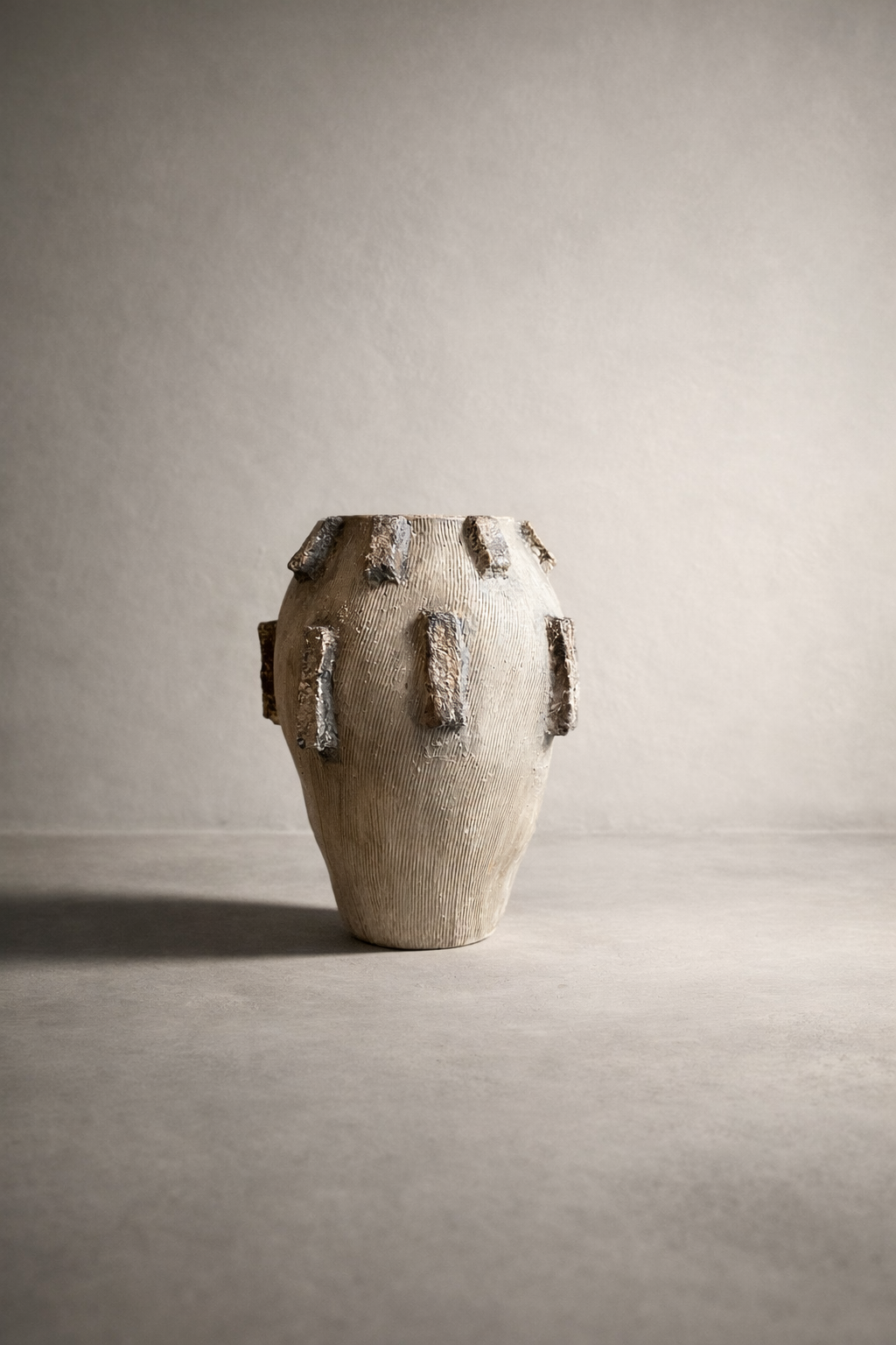 Neutral elongated vessel with raised bark-style relief accents on a textured surface