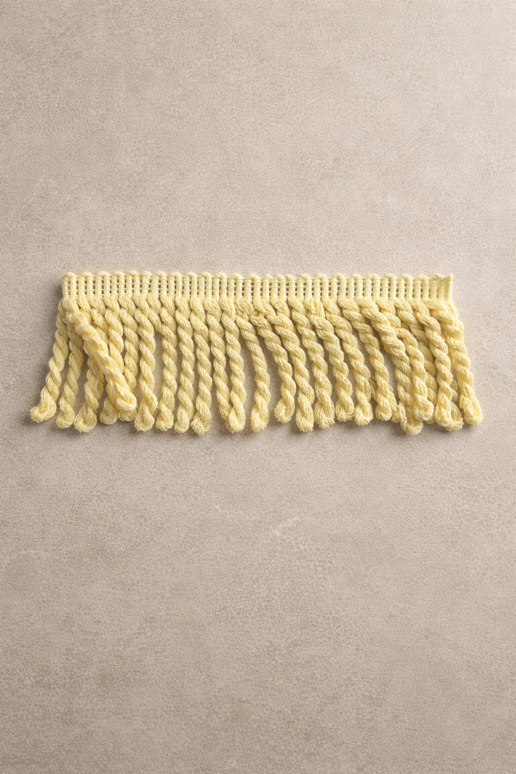 Pale yellow whipped butter fringe tissue box cover with dense twisted fringe texture in a warm neutral studio setting
