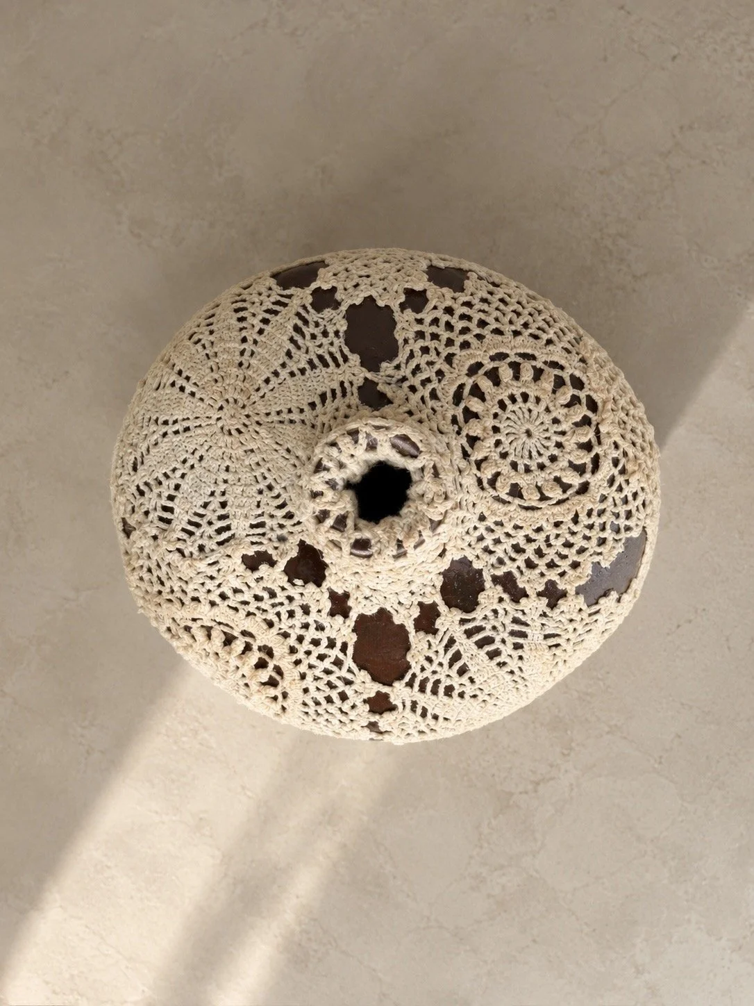 Veil Vessel by Amber Renee Hansen, a deep brown ceramic vessel wrapped in warm ivory vintage hand-crocheted lace.