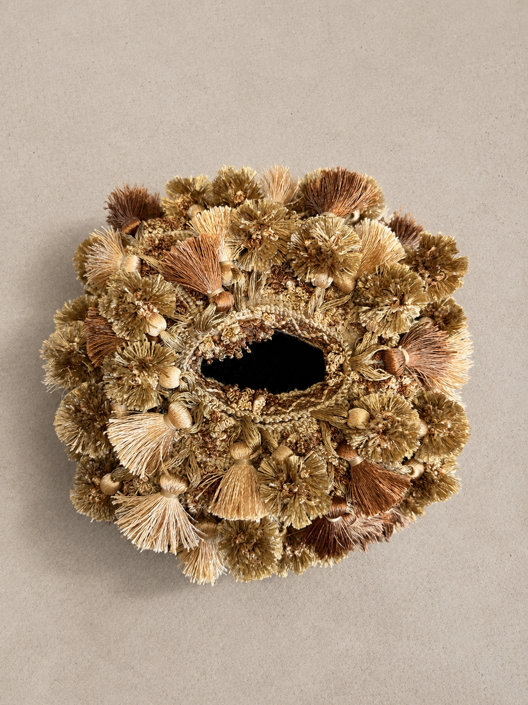 Close-up of a handcrafted tissue box cover with dense tassel fringe in varying shades of soft green, golden tan, and rich brown.
