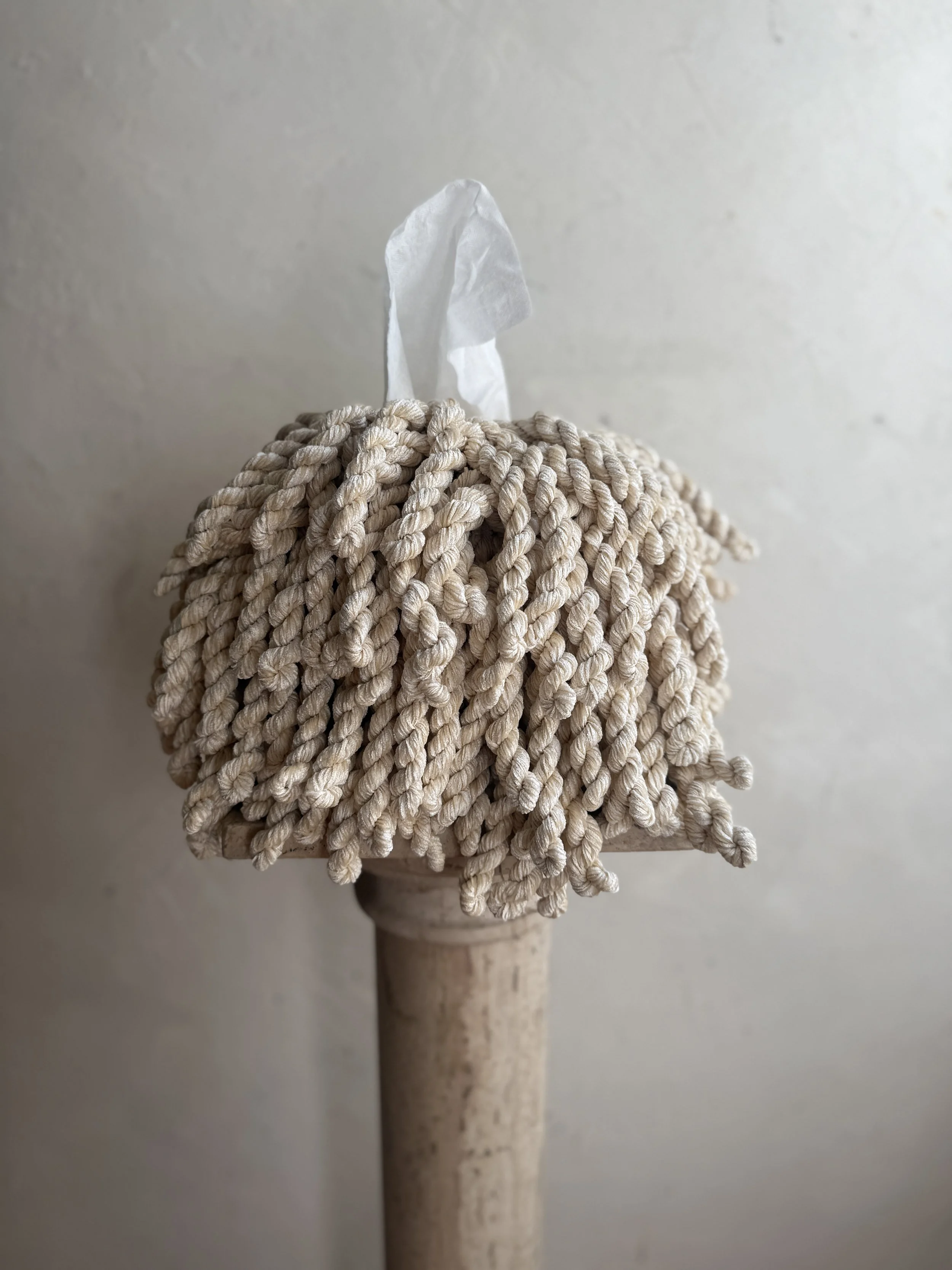 Oat Chunky Luxe Fringe Tissue Box Cover wrapped in thick twisted oat fringe, styled on a minimal plaster backdrop with stone pedestal