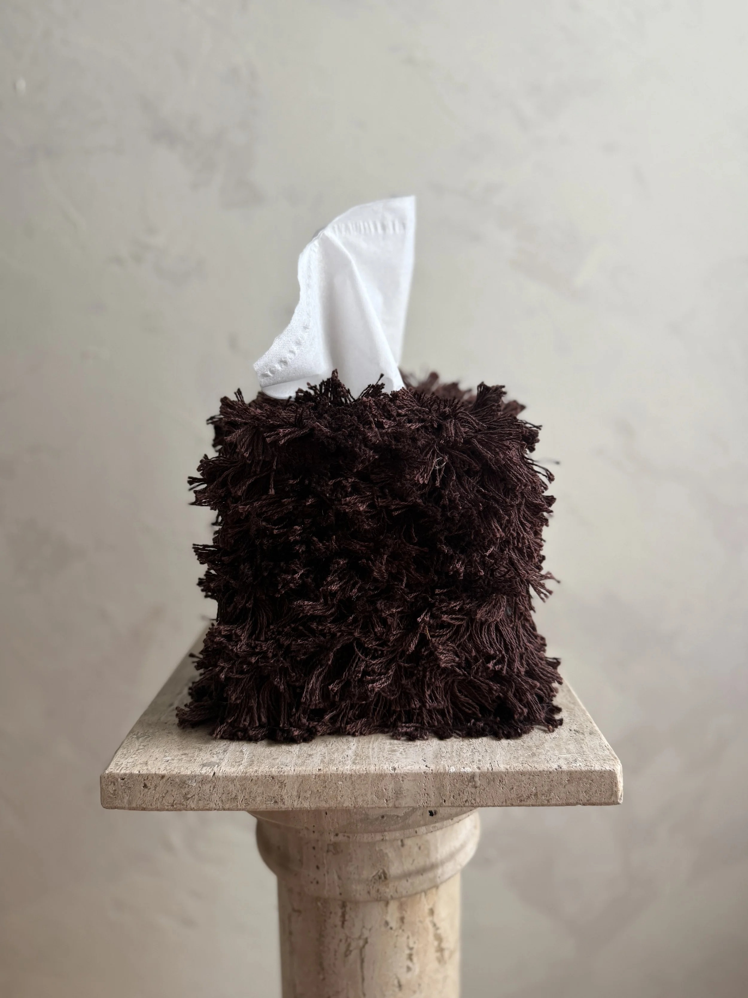 Messy Mahogany Brown fringe tissue box cover on a textured stone surface with a soft neutral wall background