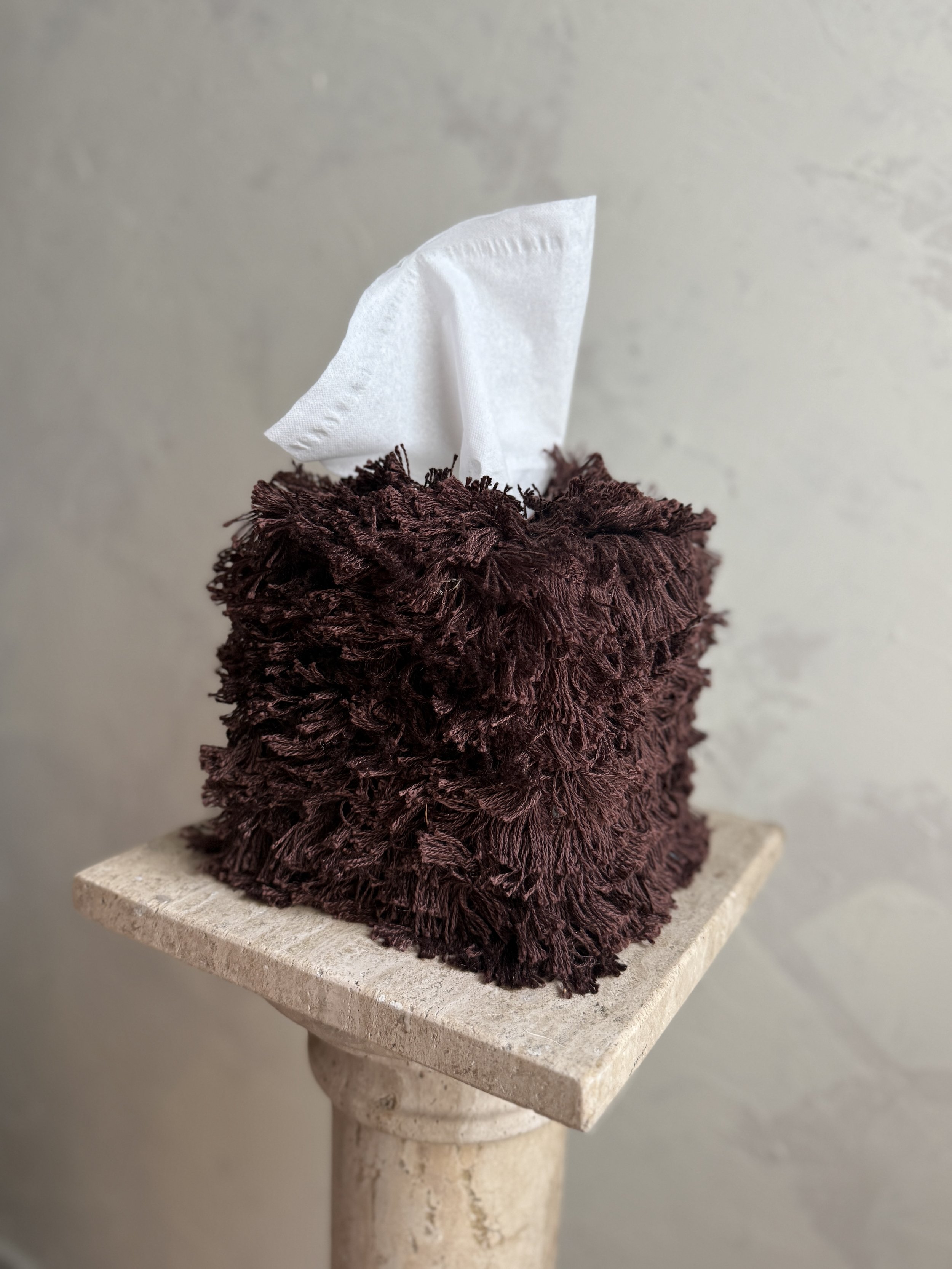 Messy Mahogany Brown fringe tissue box cover on a textured stone surface with a soft neutral wall background