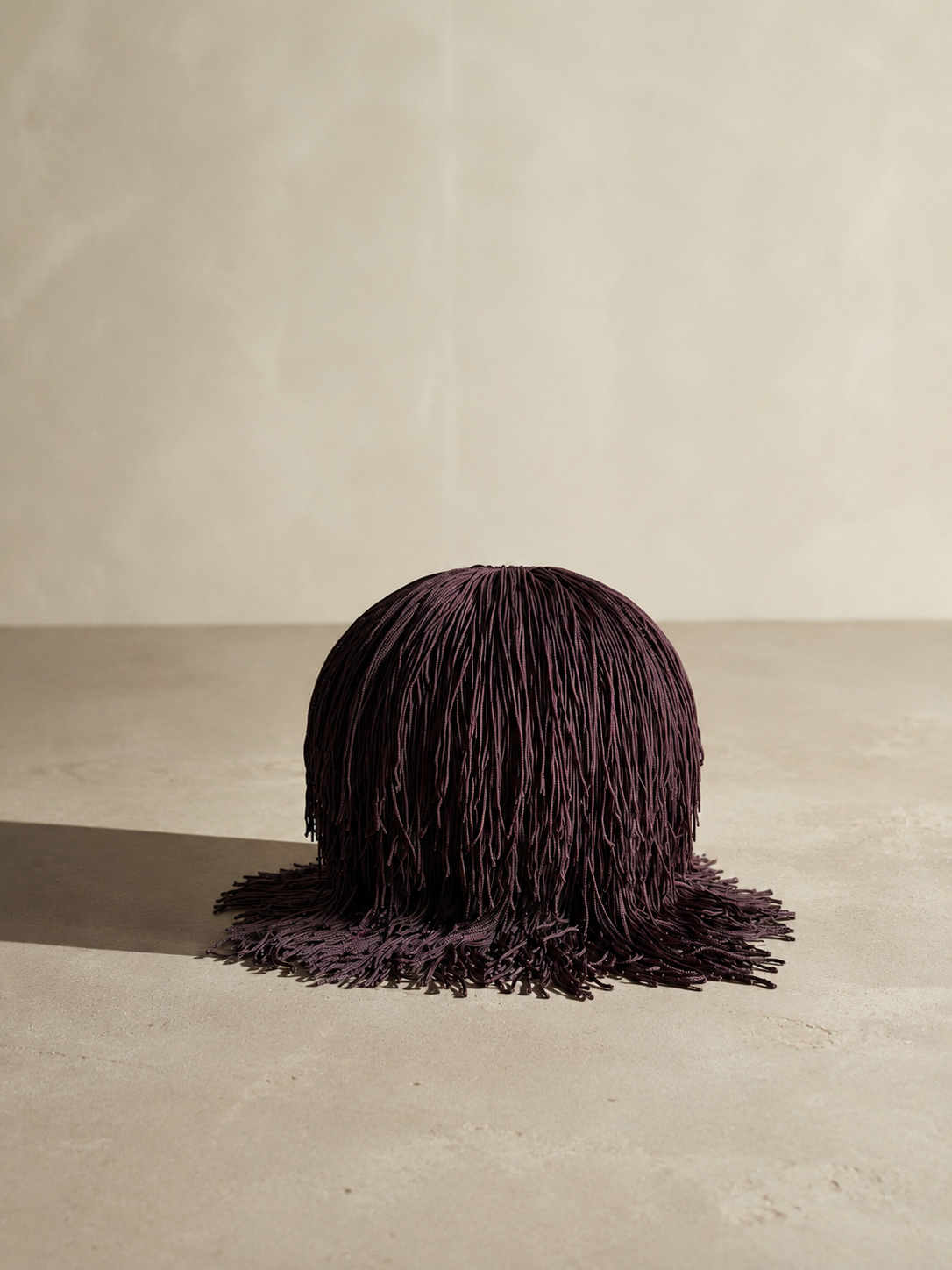 Bordeaux Noir Spill Sphere Vessel with cascading fringe holding burgundy flowers against a warm neutral background.