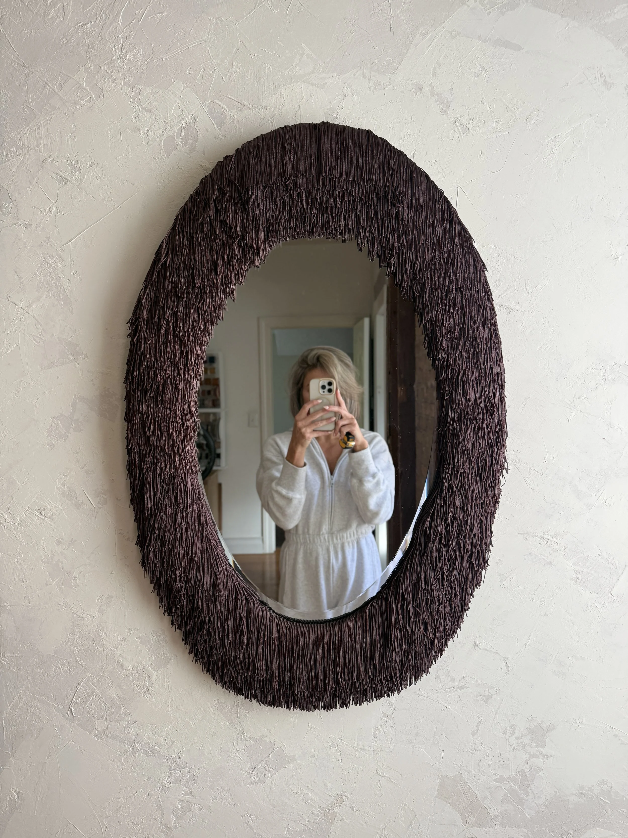 Oval mirror wrapped in rich, dimensional fringe.
