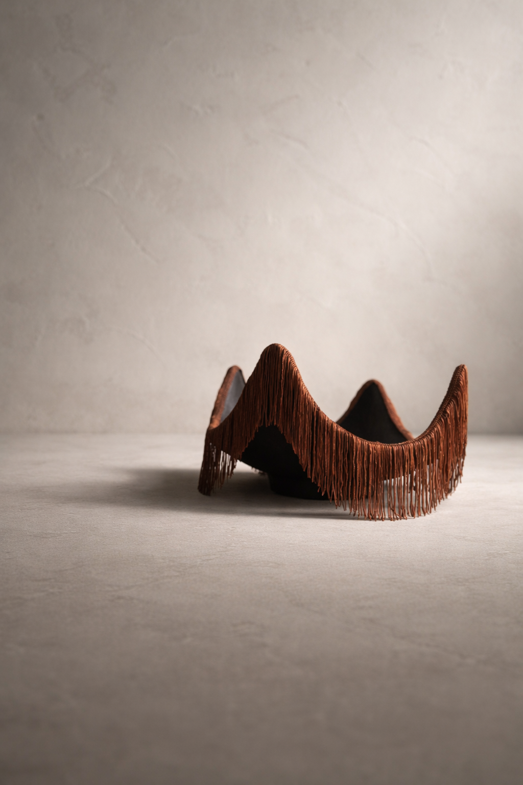 A sculptural catchall tray with a warm cayenne tone, featuring a wavy silhouette and fringe detail, set against a neutral studio background.