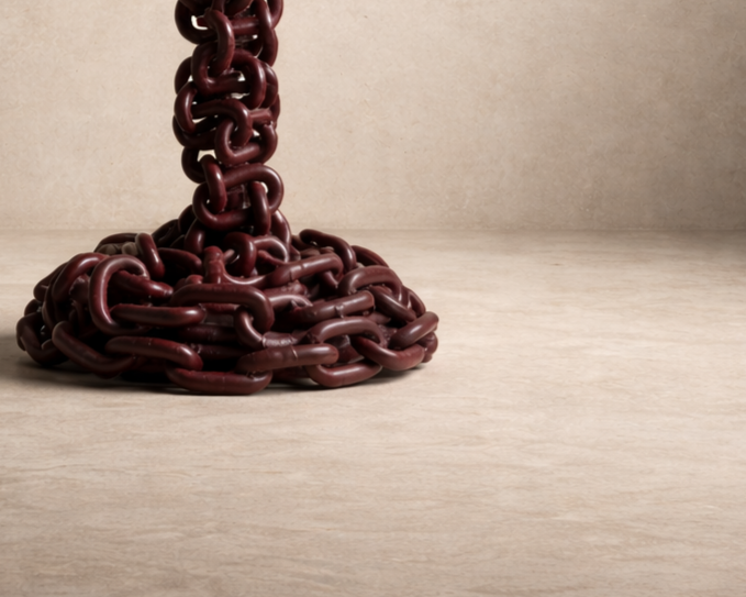 Close-up of a sculptural burgundy chain lamp base, featuring interwoven metal links with a rich, glossy finish against a neutral background.