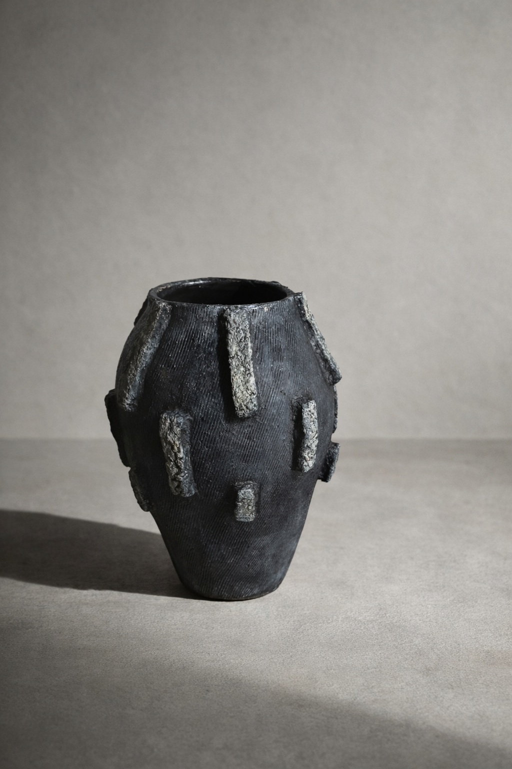 Black elongated vessel with raised bark-style relief accents and matte textured finish