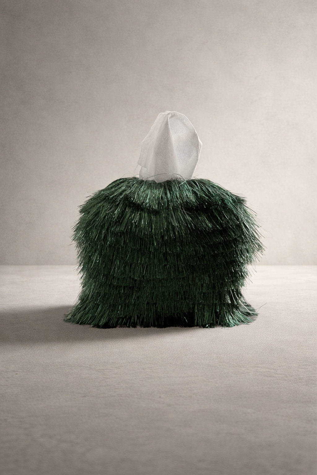 Emerald static fringe tissue box cover with dimensional tinsel strands displayed in a warm neutral editorial studio setting