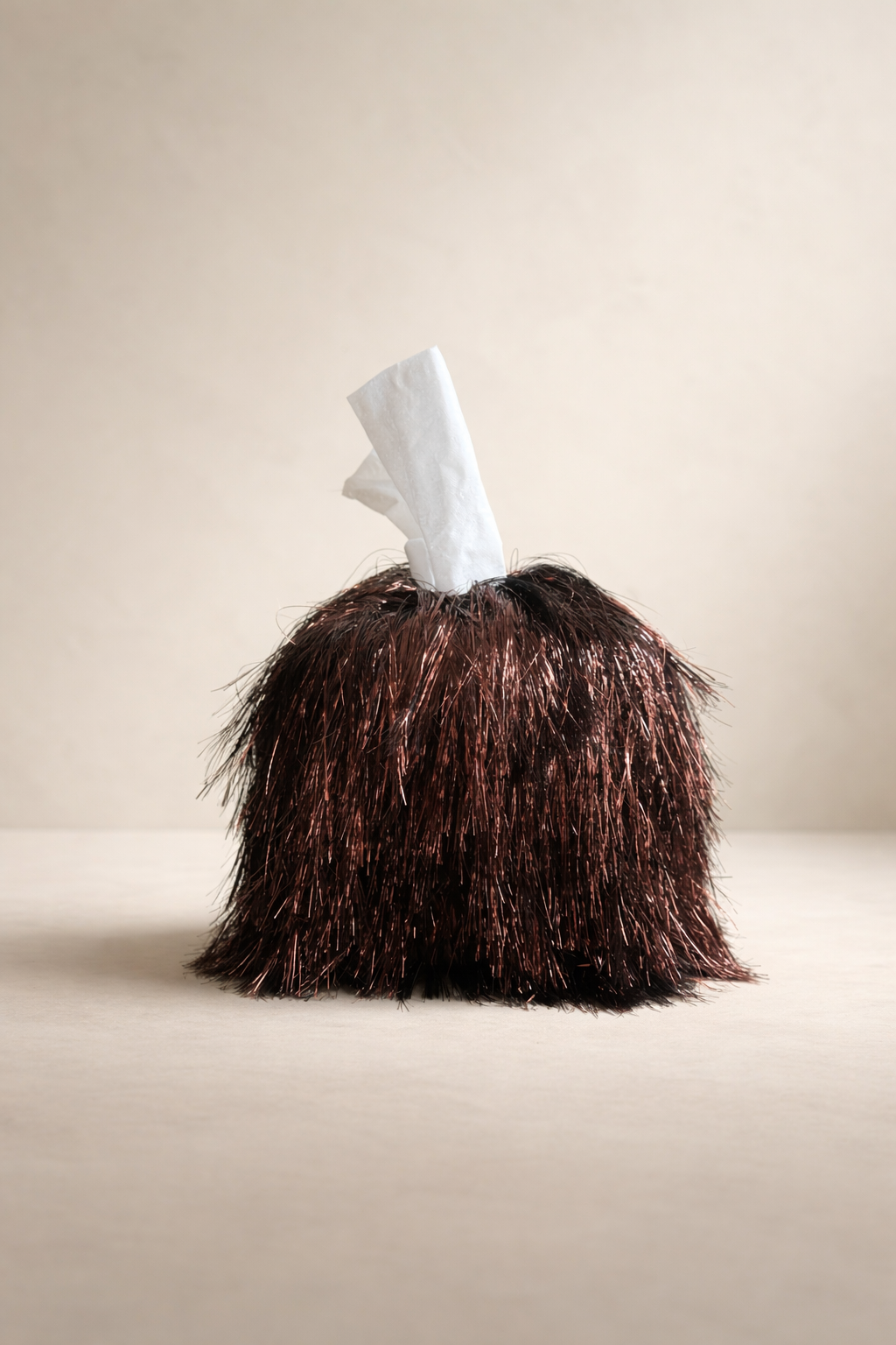 Burnt mahogany static tinsel fringe tissue box cover with reflective layered texture in a warm luxury interior