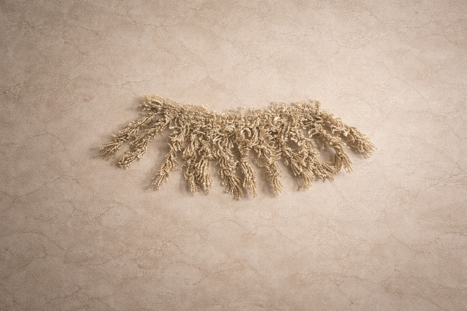 Elongated oval wall mirror wrapped in soft moss shag fringe, shown against a warm neutral plaster wall in soft natural light.