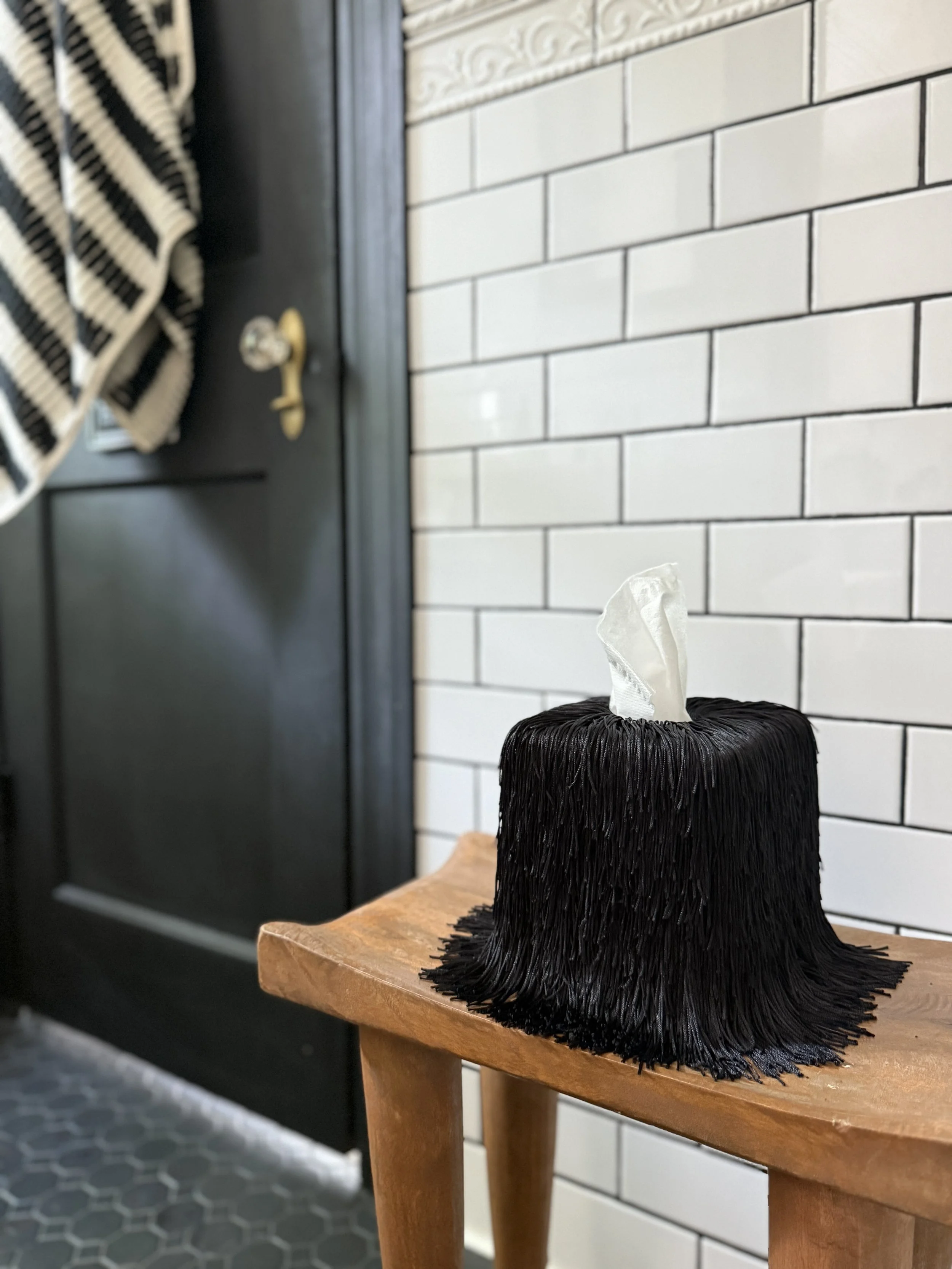 Black fringe Spill Edit tissue box cover with soft draping strands displayed on a tabletop