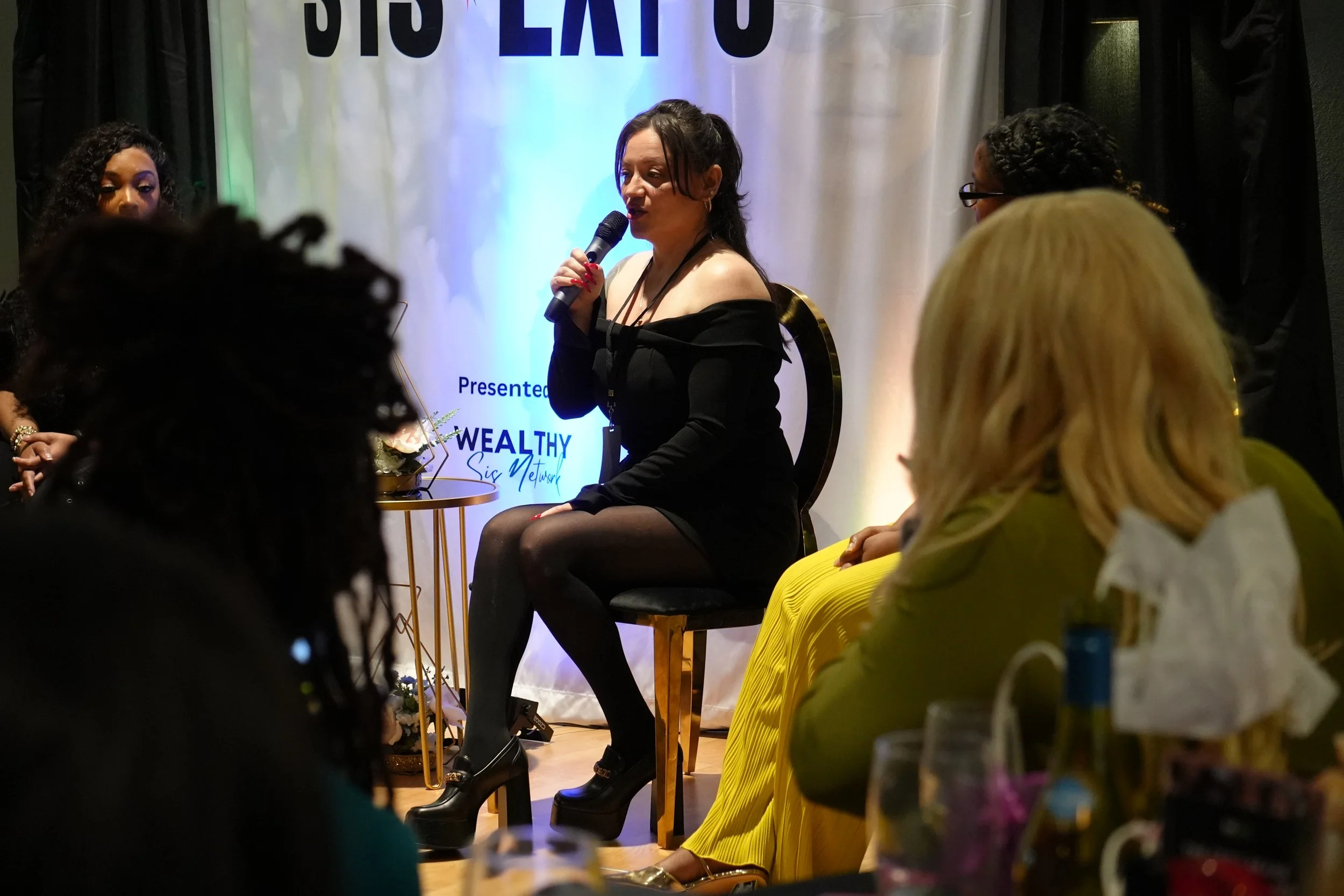 A man with dreadlocks wearing glasses and a black shirt shaking hands with another man in a pinstripe suit holding a microphone at SIS Expo