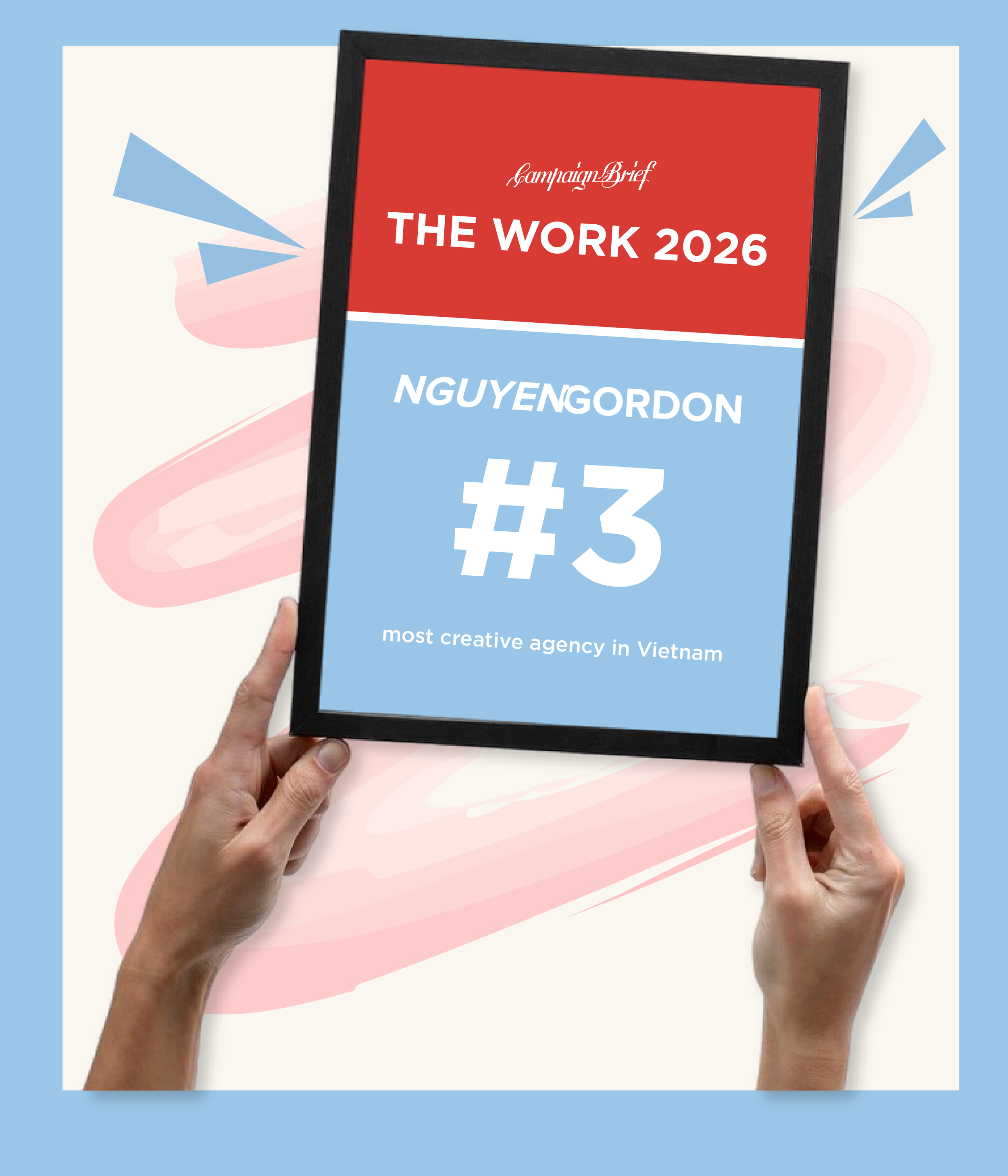 A person holding a black-framed poster with red and blue sections. The poster reads 'Campaign Brief THE WORK 2026 NGUYENGORDON #3' and is described as the most creative agency in Vietnam.