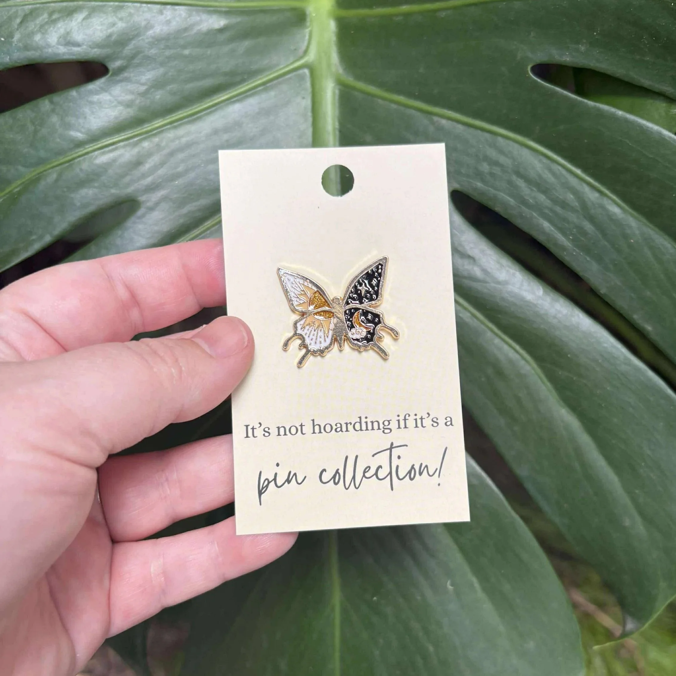 Butterfly enamel pin with one wing showing the sun and the other wing featuring the moon and stars.