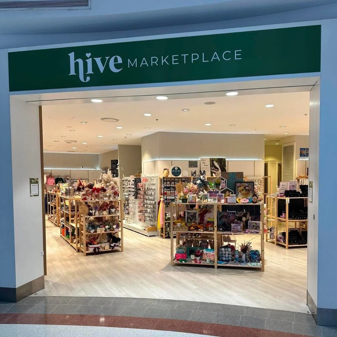 Inside view of Hive Marketplace, a retail store with shelves displaying various products including accessories, decorations, and gift items, under bright ceiling lights.